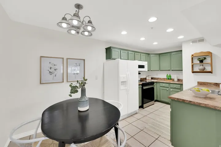Kitchen with green cabinetry, white appliances, light tile patterned floors, light countertops, and hanging lights