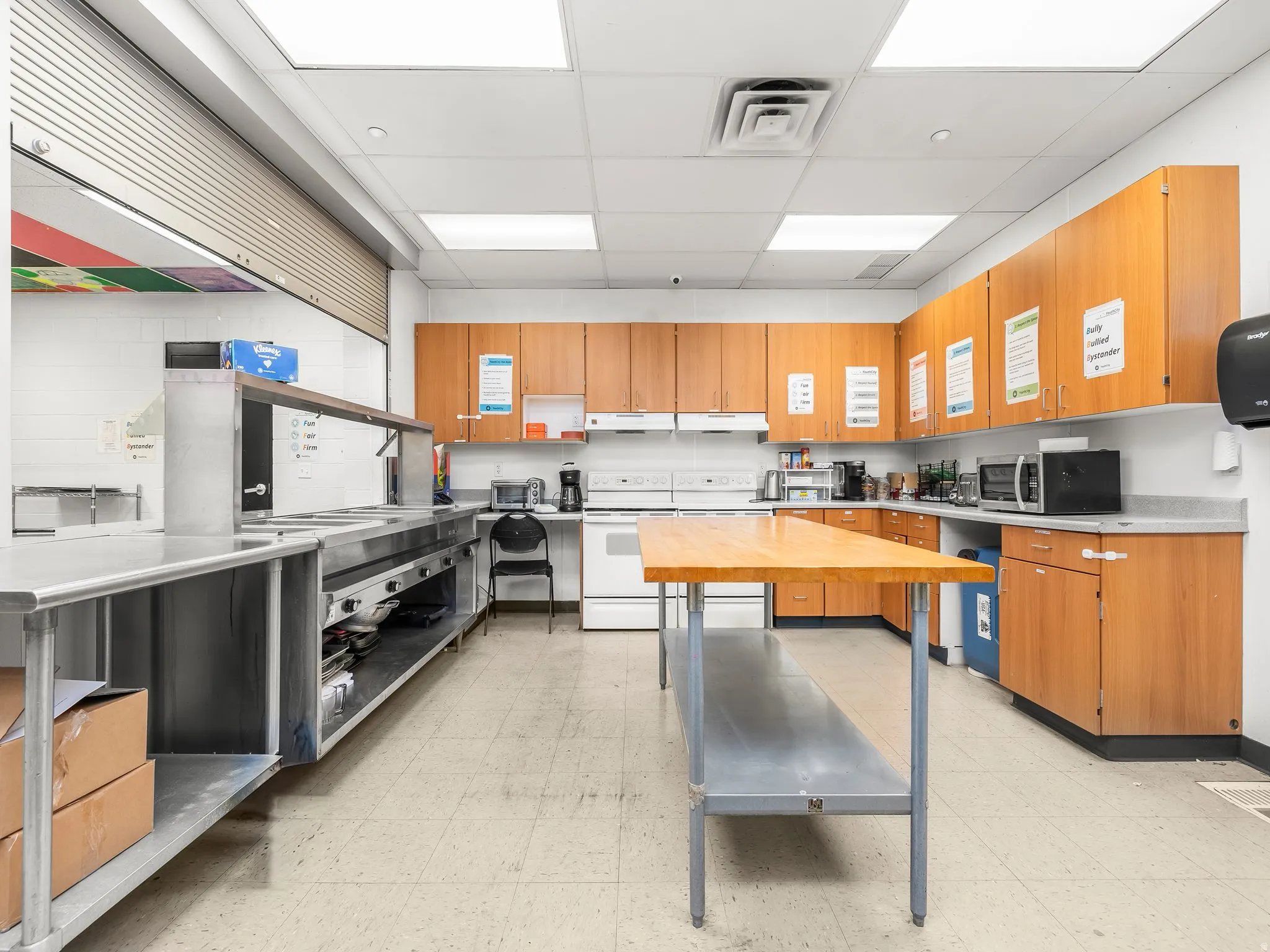 Kitchen with a paneled ceiling, white electric range, stainless steel microwave, stainless steel countertops, and dual tone cabinets