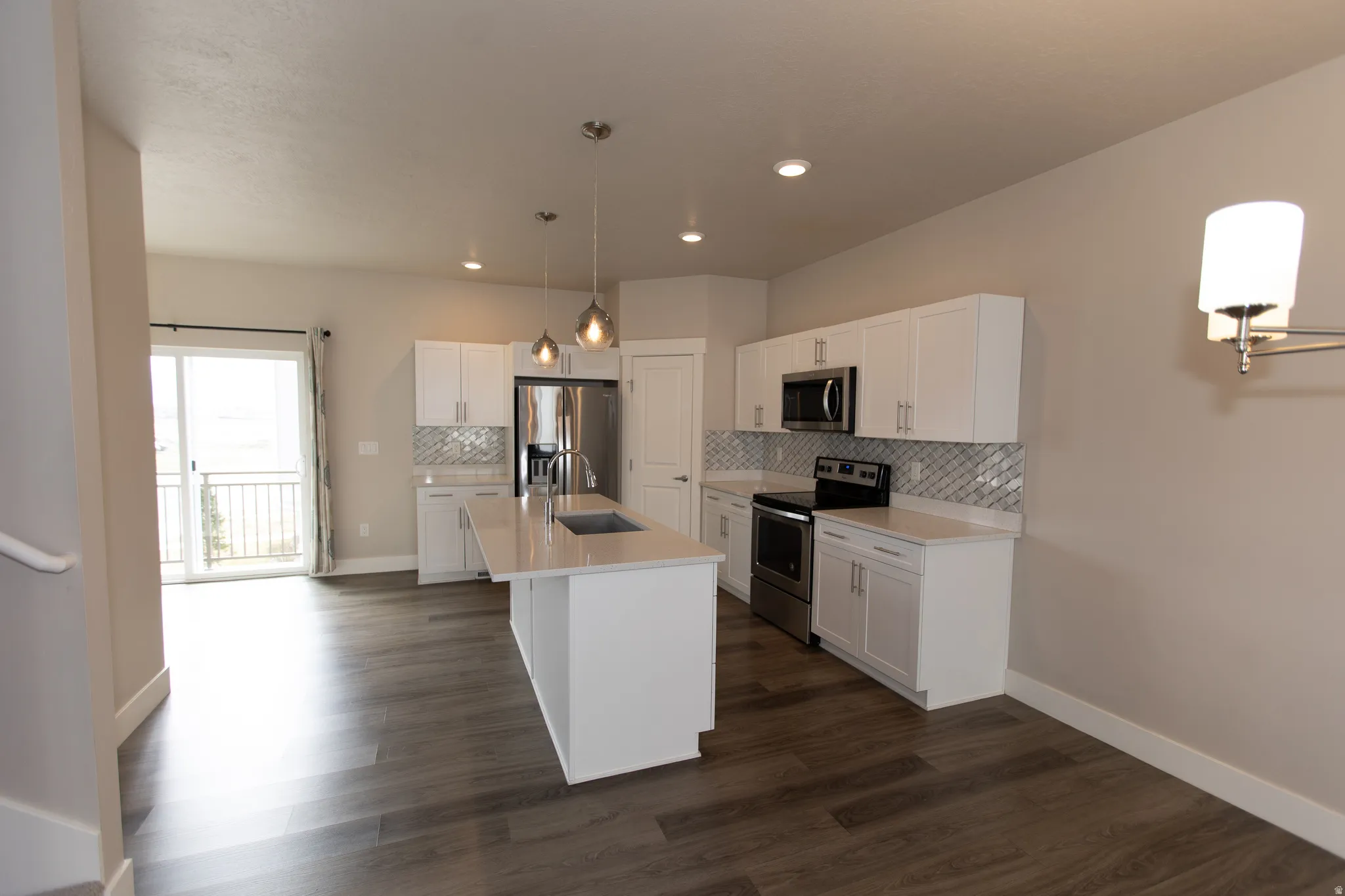 Kitchen featuring white cabinetry, stainless steel appliances, tasteful backsplash, a kitchen island with sink, and dark wood finished floors