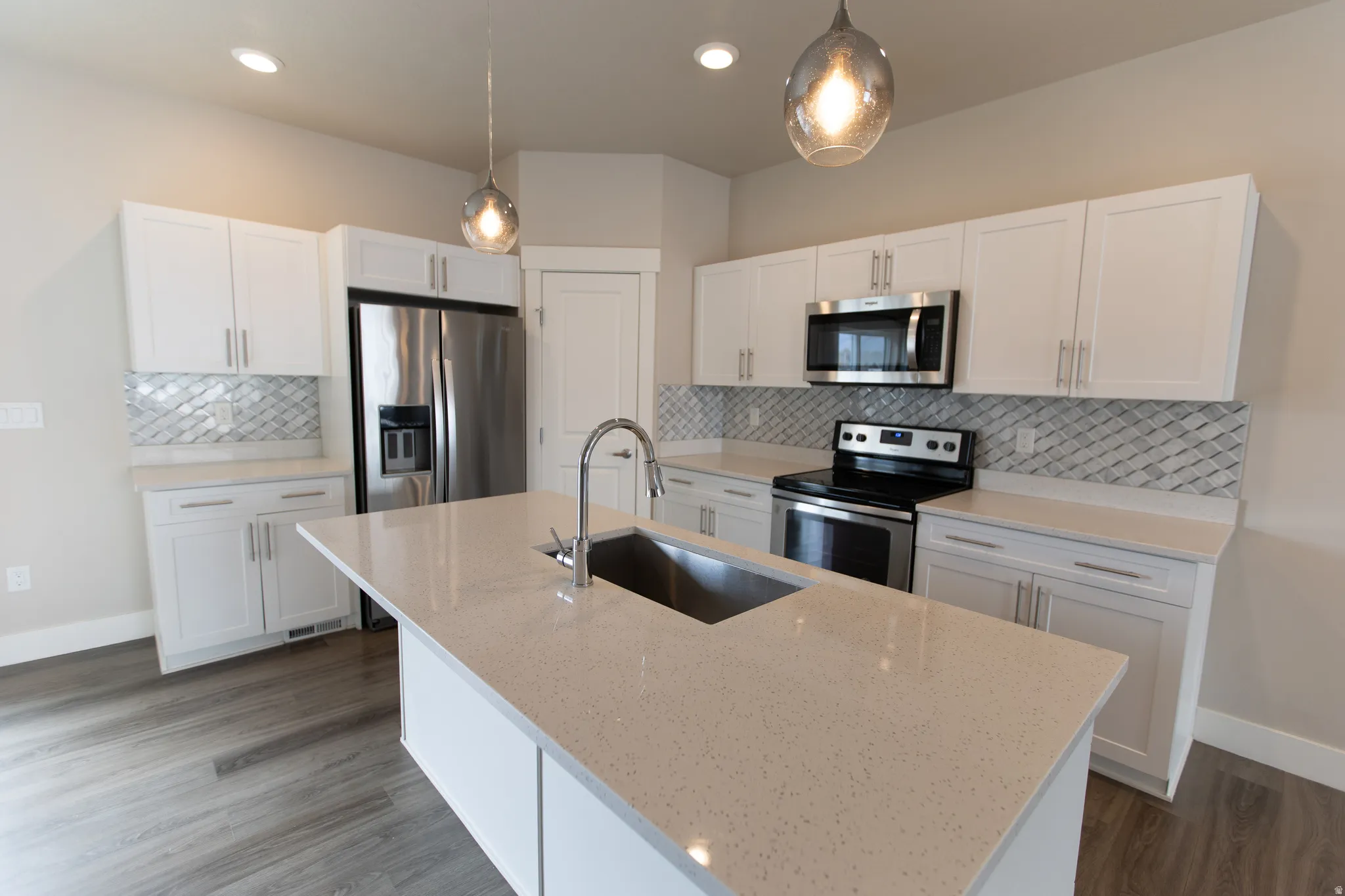 Kitchen featuring stainless steel appliances, white cabinetry, and hanging light fixtures