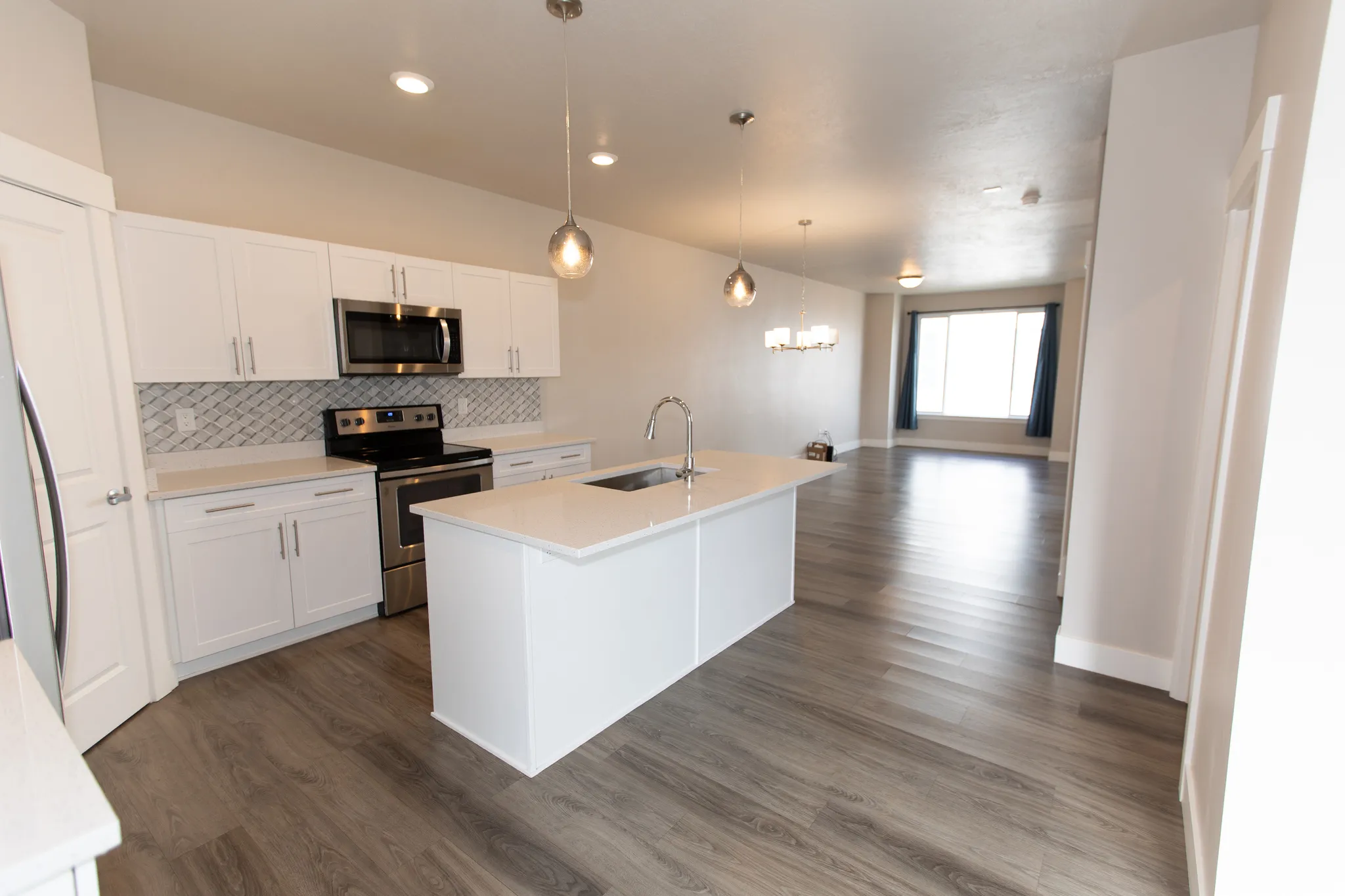 Kitchen with stainless steel appliances, a kitchen island with sink, white cabinets, dark wood finished floors, and a chandelier
