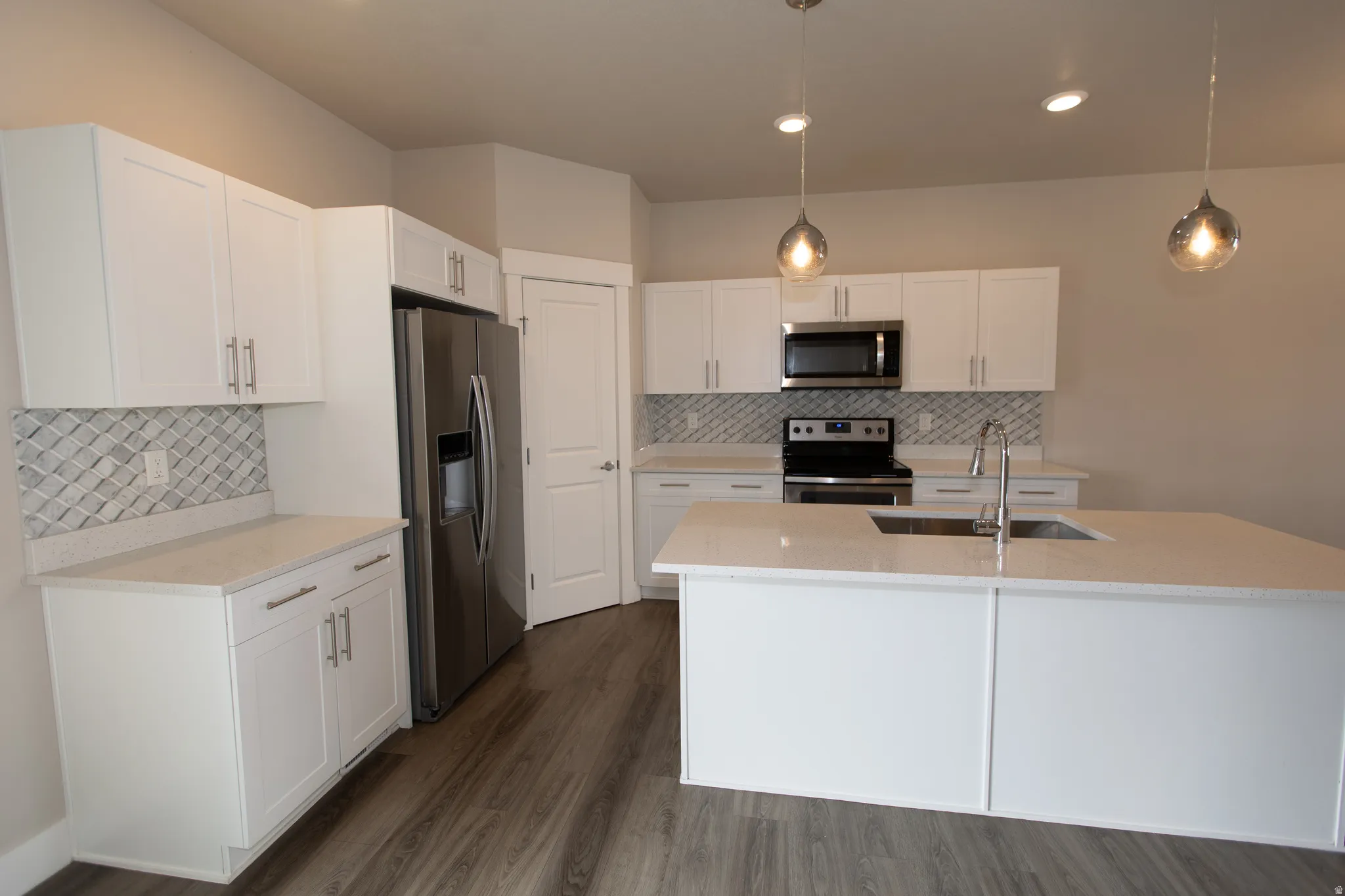 Kitchen featuring stainless steel appliances, white cabinets, dark wood-style flooring, a center island with sink, and hanging light fixtures