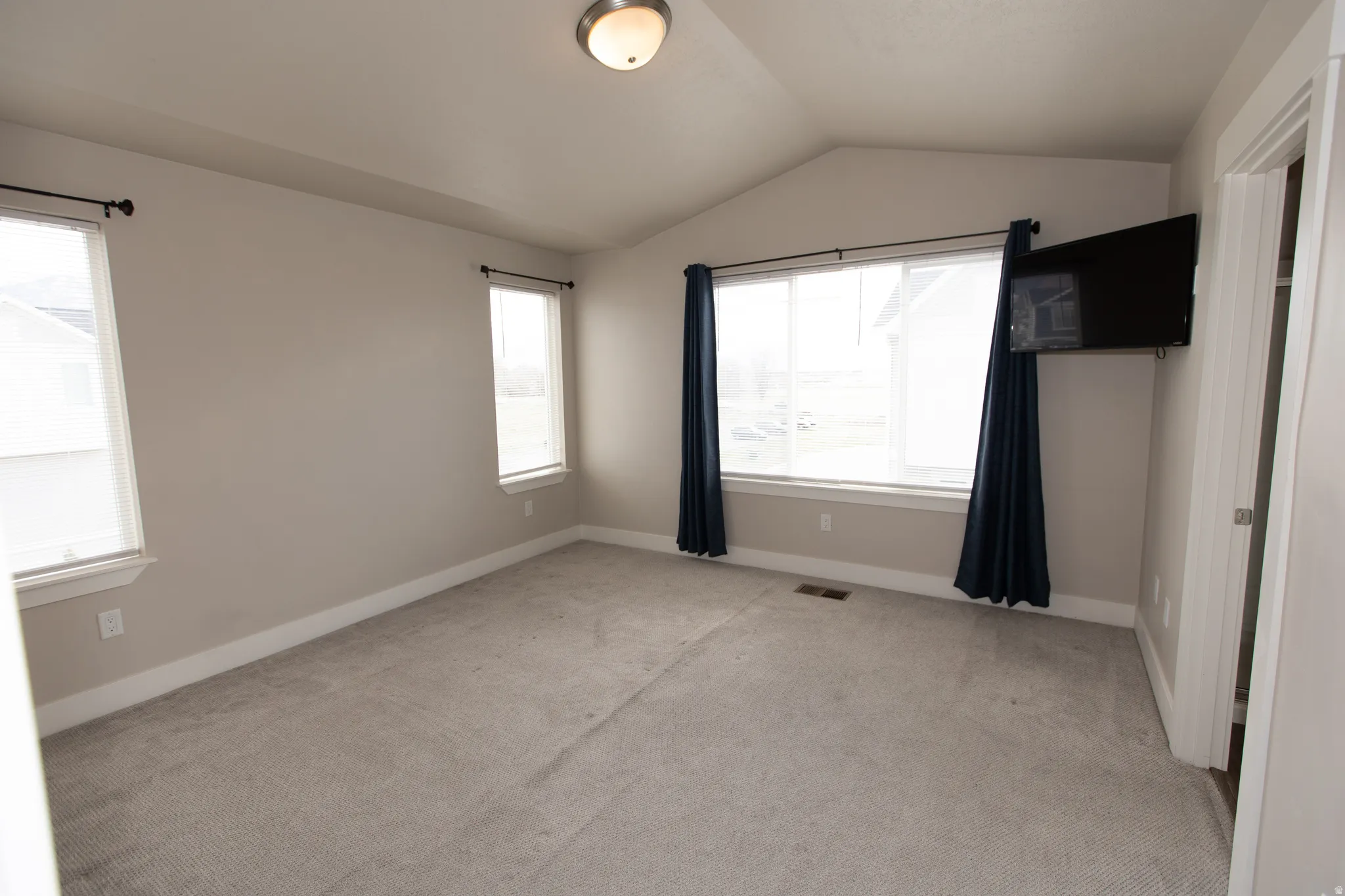Unfurnished bedroom with light colored carpet and multiple windows