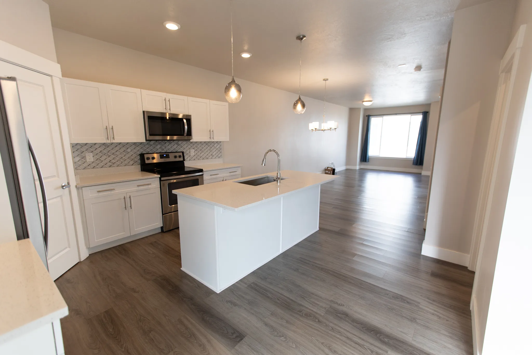 Kitchen with stainless steel appliances, white cabinetry, a center island with sink, dark wood finished floors, and suspended lighting