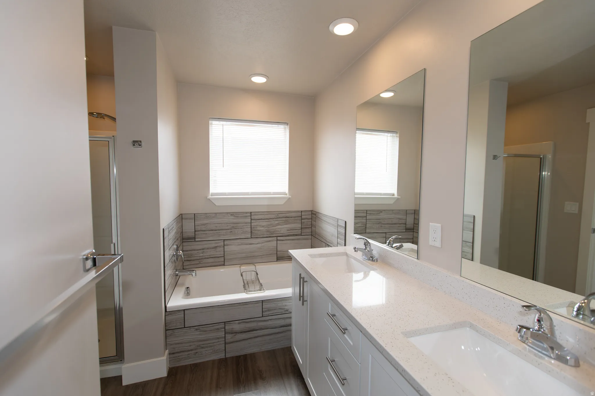 Bathroom with double vanity, a shower stall, a garden tub, dark wood-style flooring, and recessed lighting