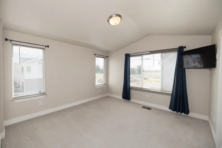 Vaulted ceiling, neutral wall paint, light-colored carpeting, multiple windows, and a flush-mount ceiling light