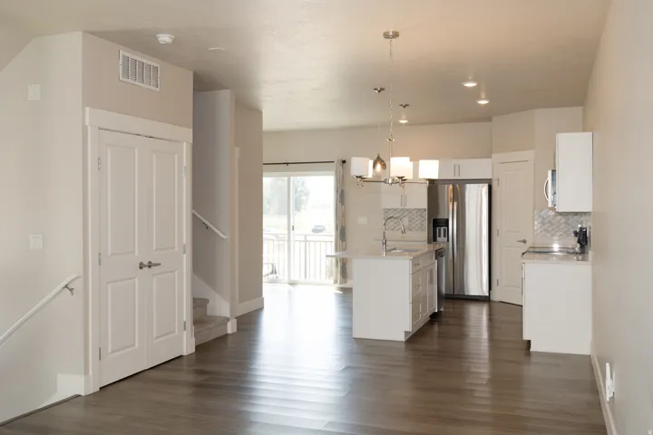 Open-concept space featuring wood-finish flooring, a kitchen island with sink, white shaker cabinetry, and stainless steel appliances