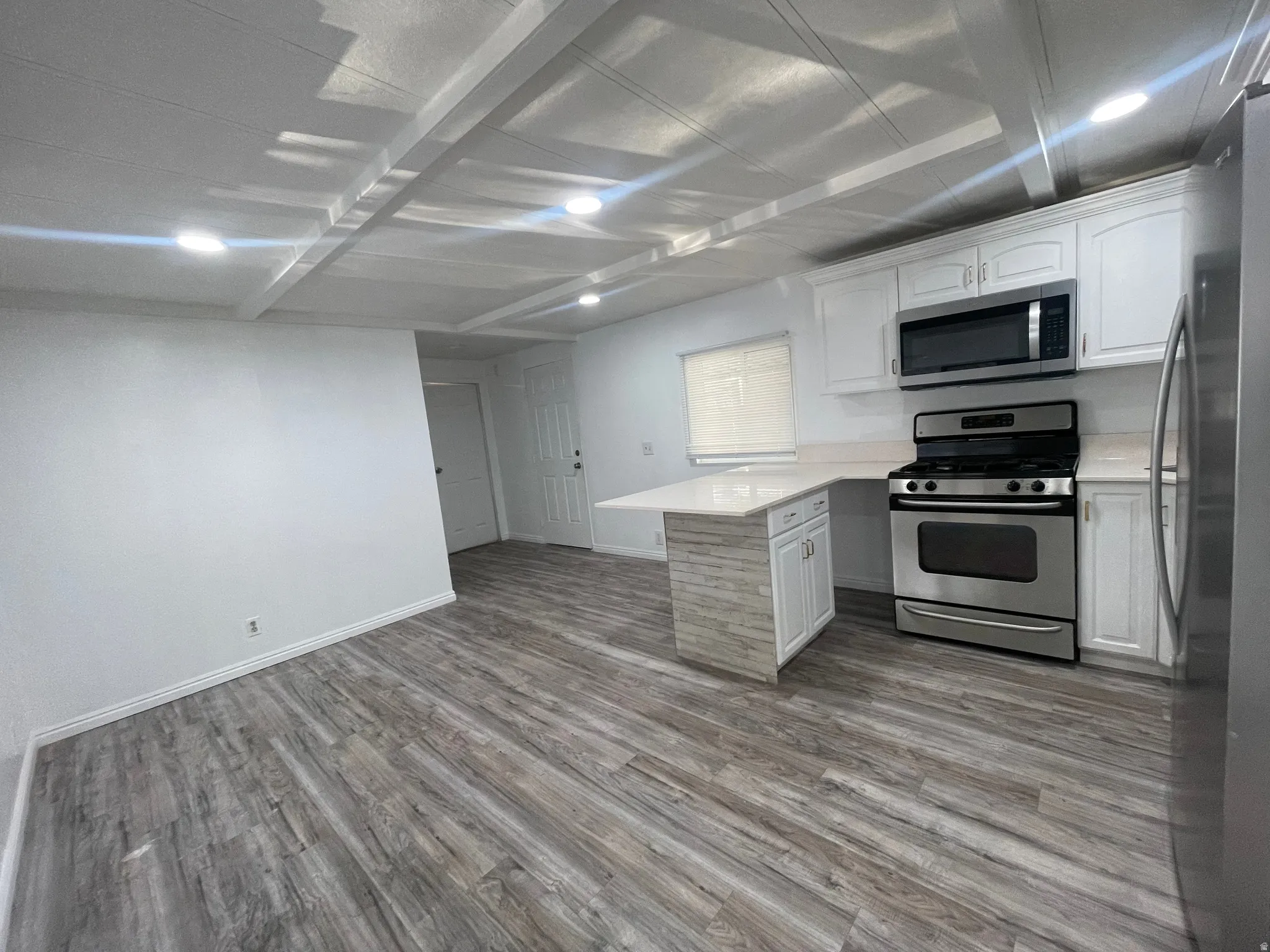 Kitchen featuring a peninsula, stainless steel appliances, white cabinets, and dark wood-type flooring