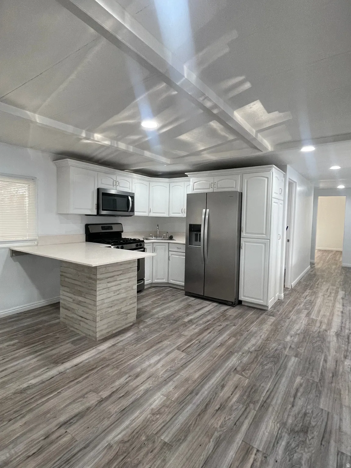 Kitchen featuring a peninsula, stainless steel appliances, white cabinets, light countertops, and recessed lighting