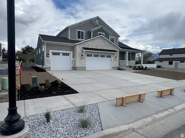 Craftsman-style home featuring a garage, stone siding, driveway, and a porch