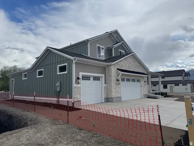 View of side of home featuring board and batten siding, stone siding, driveway, and a garage