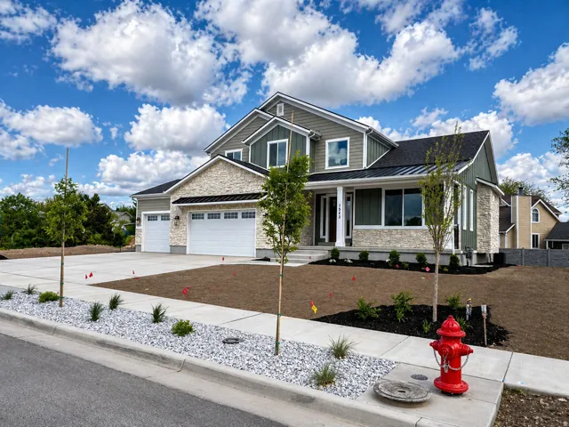 Craftsman inspired home featuring a standing seam roof, covered porch, stone siding, an attached garage, and driveway