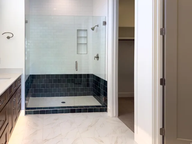 Full bath with a stall shower, vanity, light marble finish floors, and a spacious closet