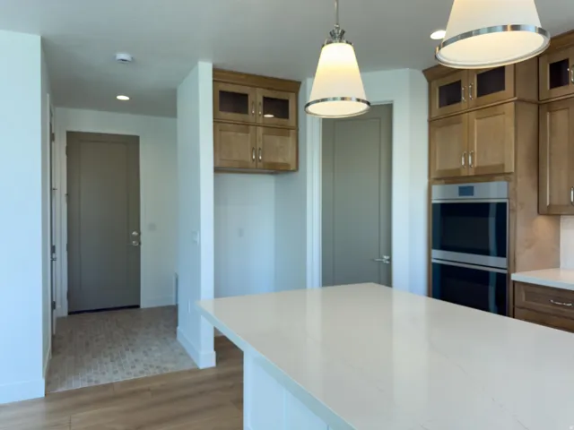 Kitchen featuring stainless steel double oven, glass insert cabinets, light wood-style flooring, and light stone counters