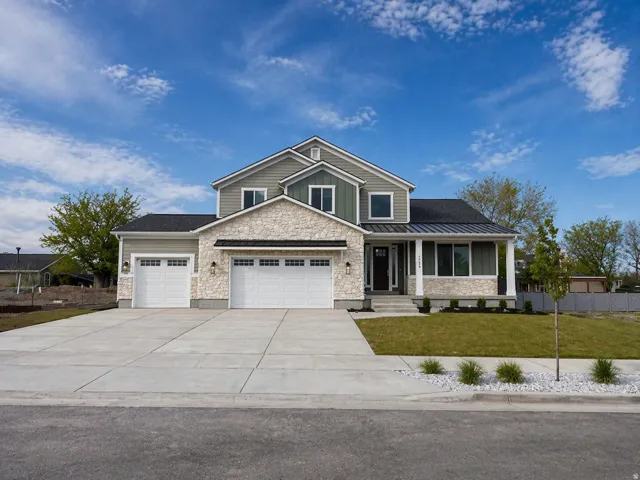 Craftsman-style home featuring stone siding, an attached garage, covered porch, concrete driveway, and a standing seam roof