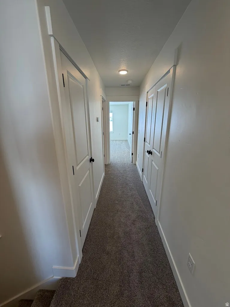 Hall featuring baseboards and dark carpet