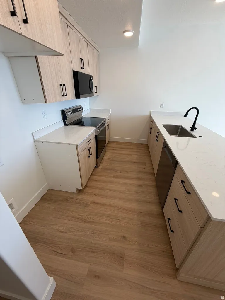 Kitchen with a peninsula, stainless steel appliances, light stone countertops, light wood-style floors, and modern cabinets