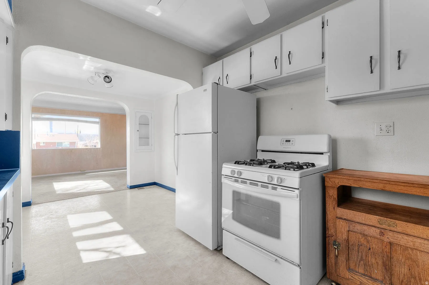 Kitchen with white gas range oven, white refrigerator, white cabinets, and arched walkways.