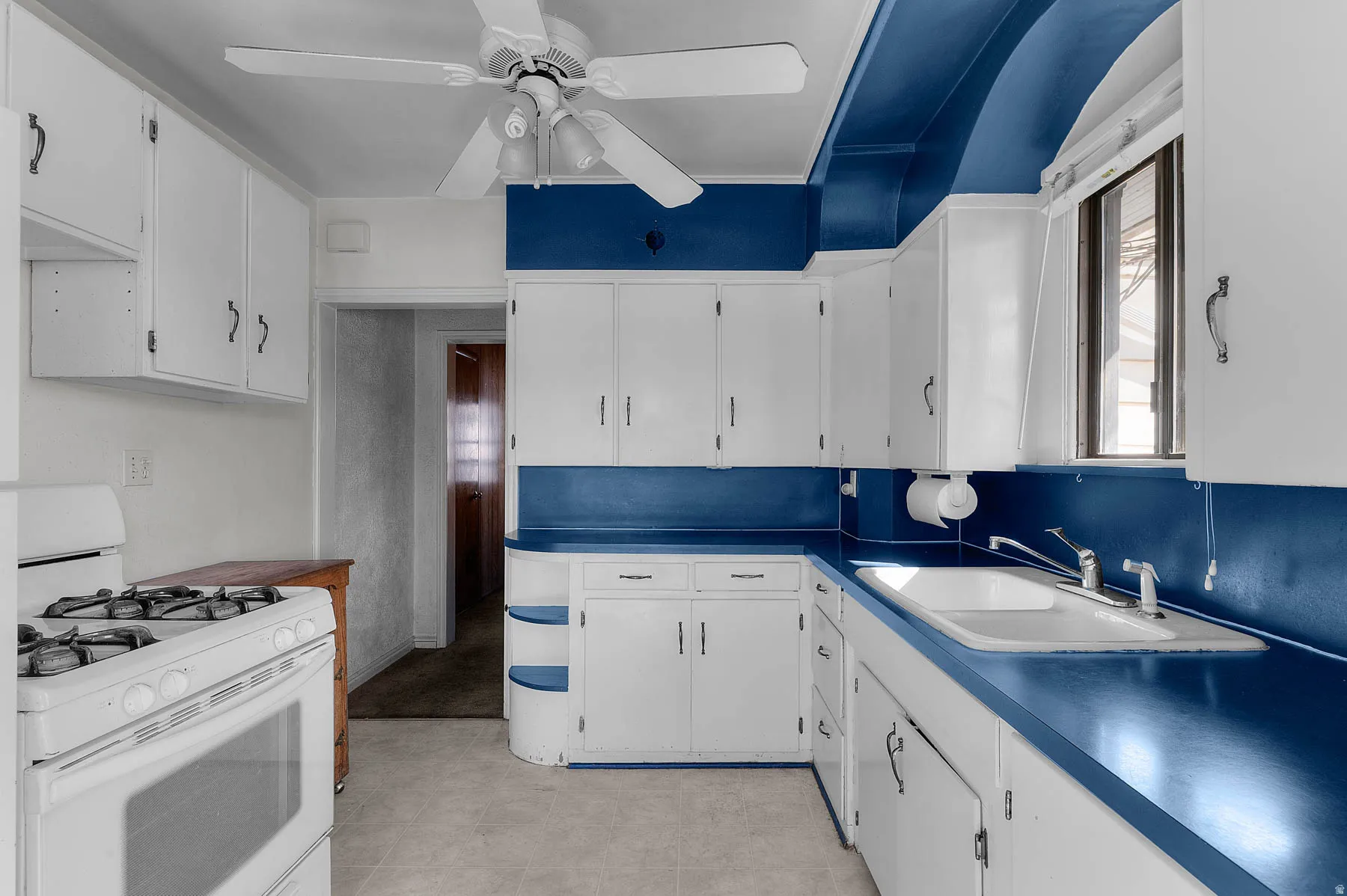 Kitchen featuring white gas stove, white cabinets, and ceiling fan.