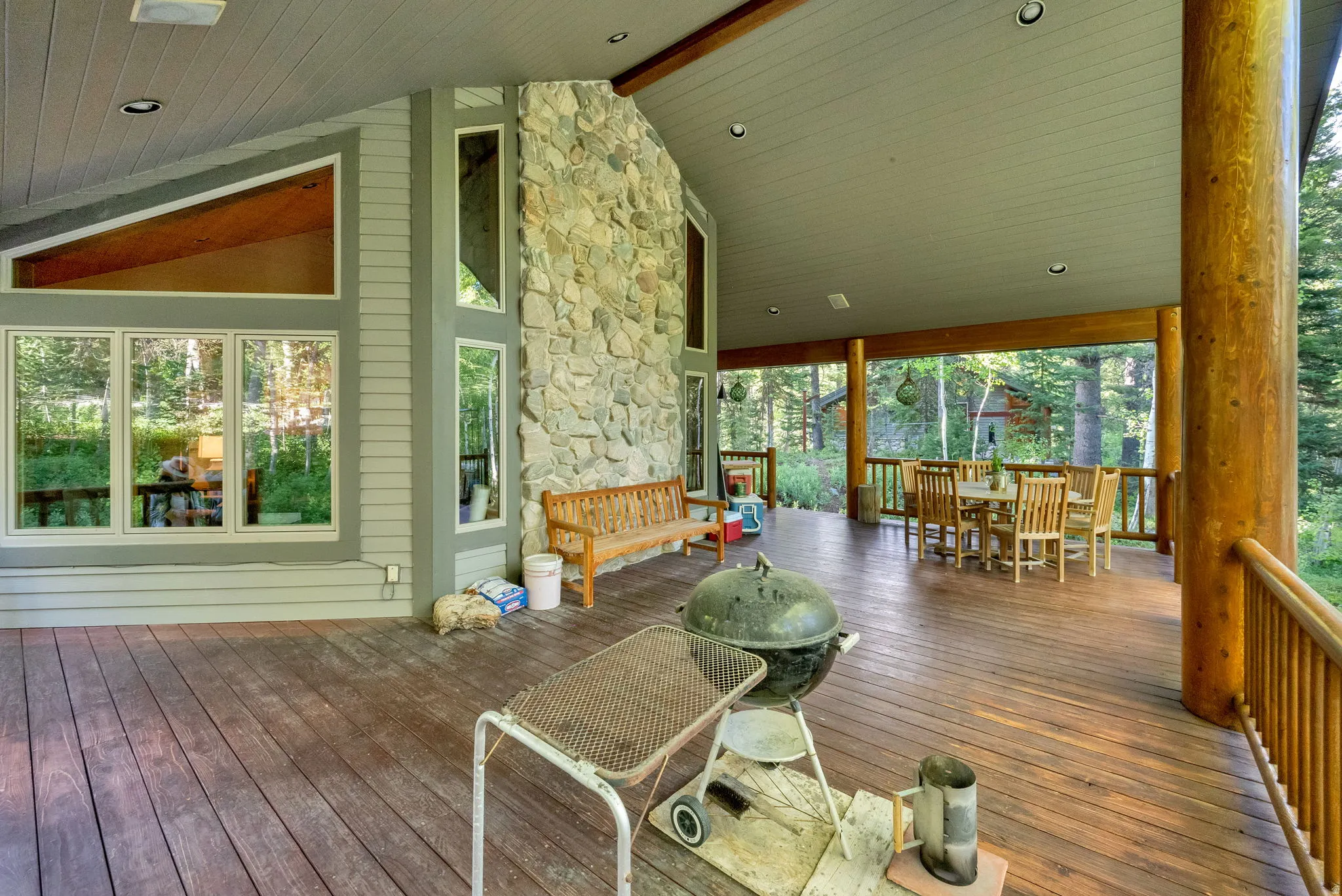 Expansive covered deck featuring wood-finish flooring, a stone accent wall, and multiple window placements