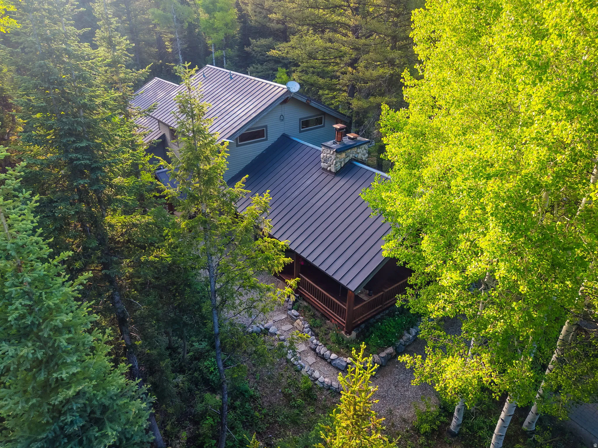 Mountain-style residence featuring a dark metal roof, natural stone chimney, and an inviting covered porch