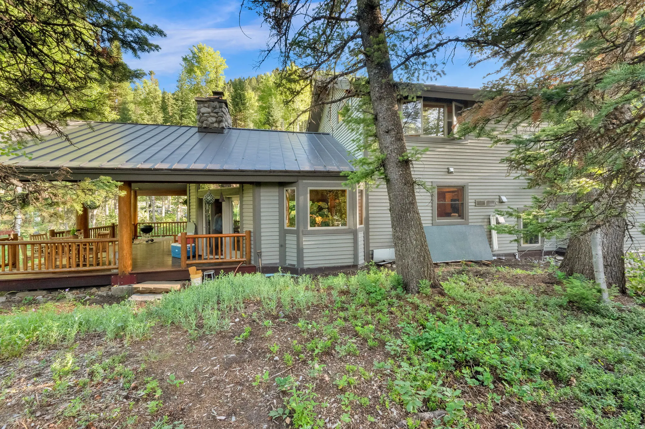 Wooded exterior featuring a covered deck with natural wood railing, a stone chimney, and a metal roof
