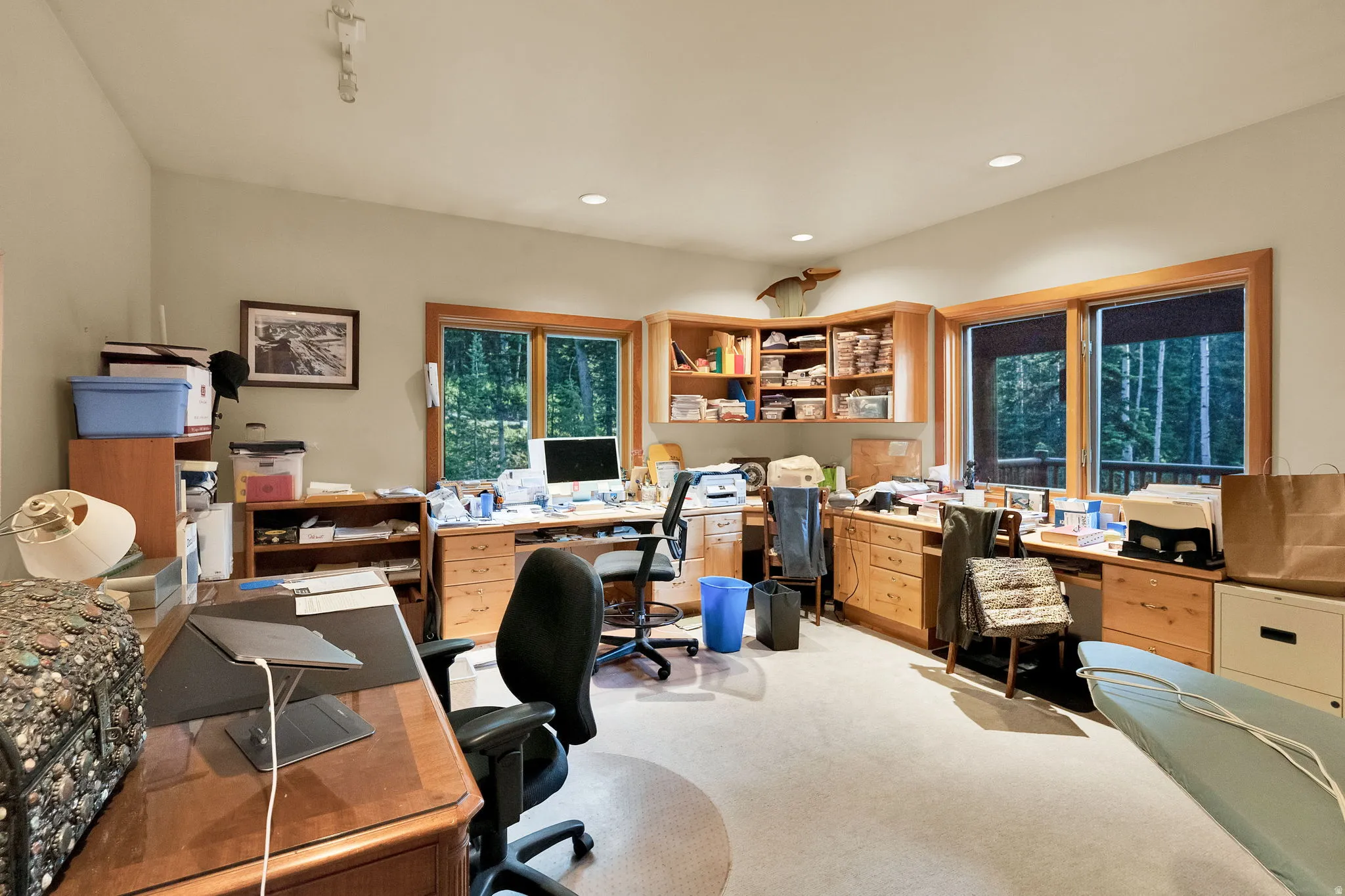 Spacious room featuring multiple built-in desks, extensive wood cabinetry with open shelving, recessed lighting, and large windows with wood trim