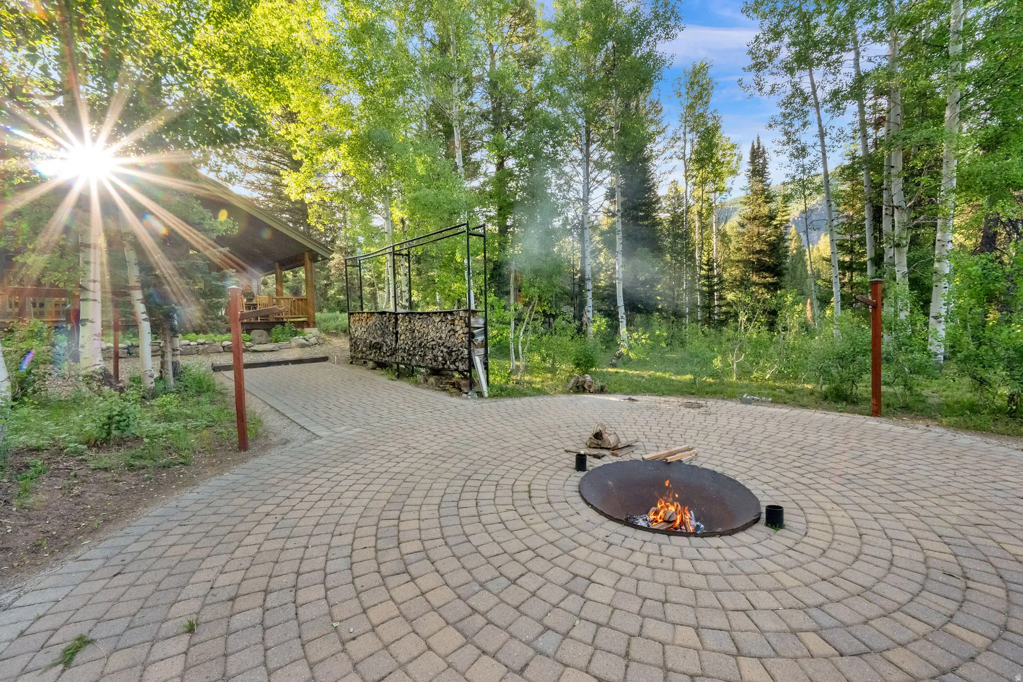 Circular paver patio with a built-in fire pit, surrounded by mature trees