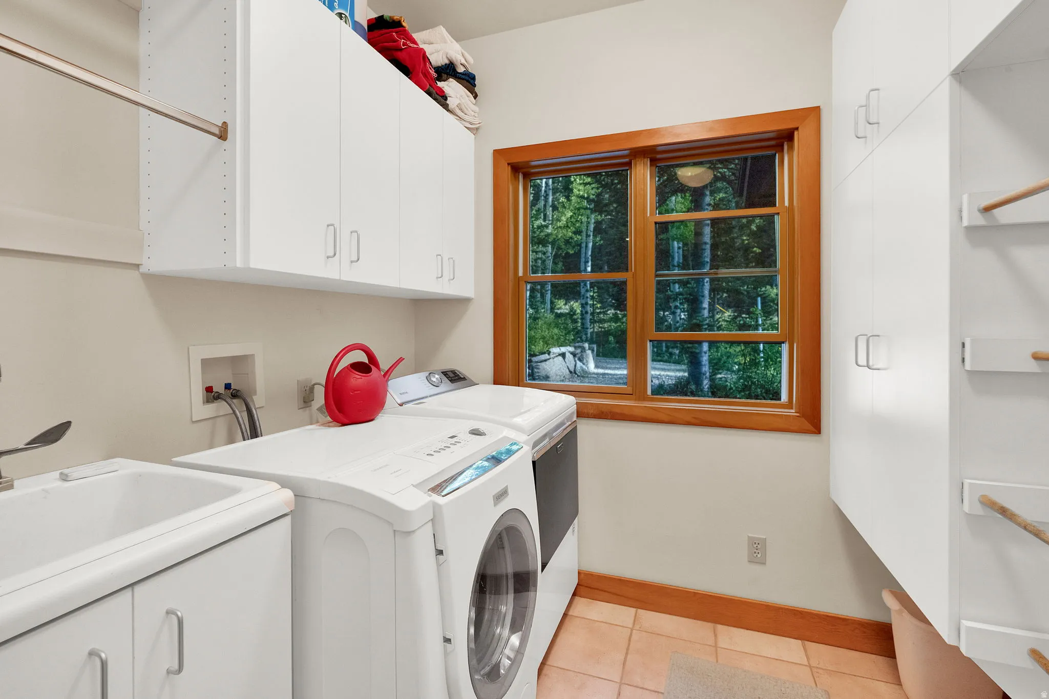 Laundry room with a utility sink, white cabinetry, a wood-framed window, and tile flooring