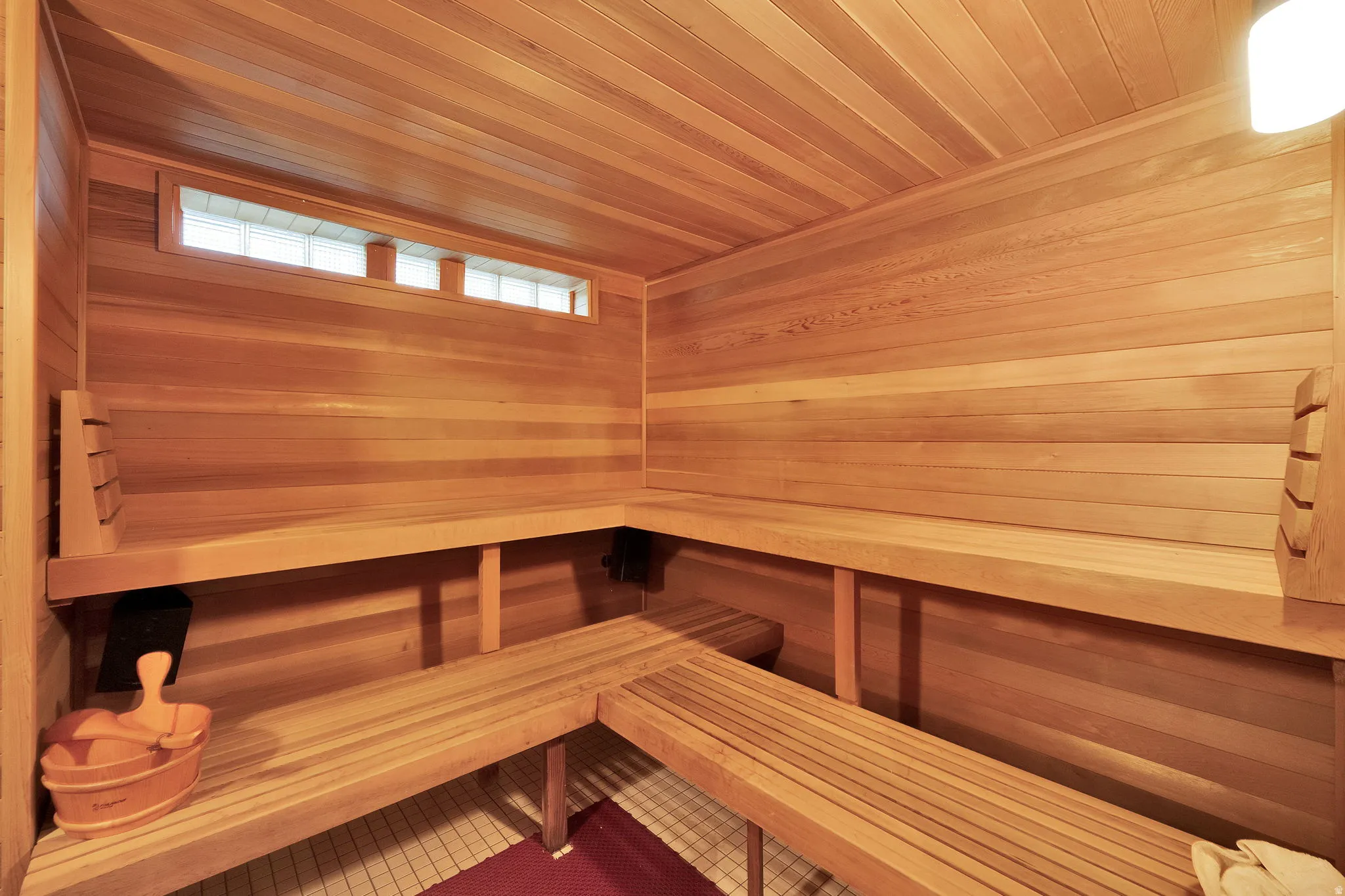 Dedicated sauna featuring light wood paneling, multi-tiered bench seating, a high transom window, and built-in lighting