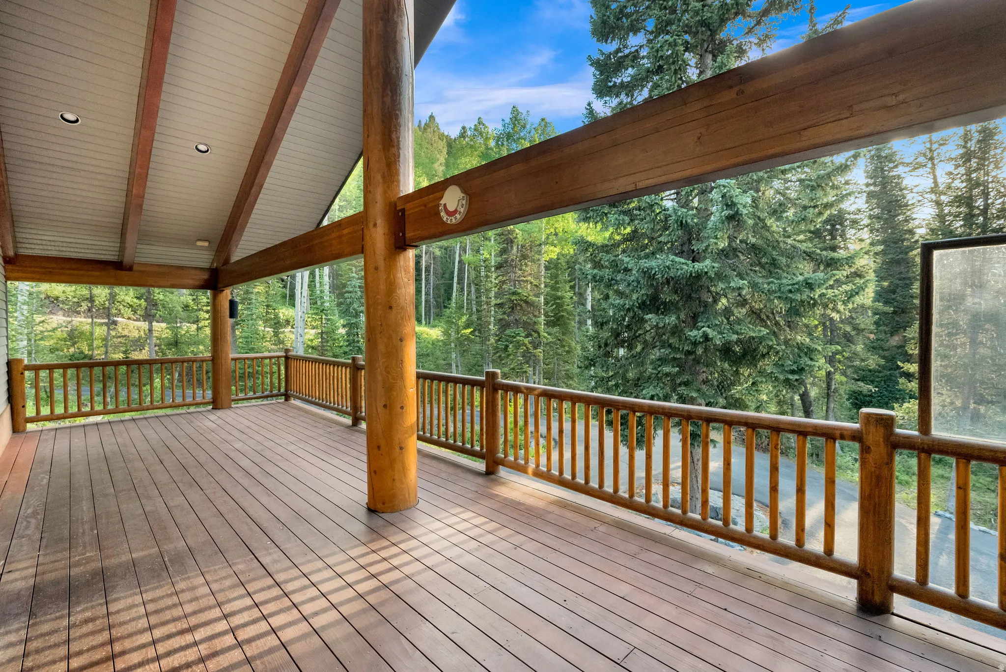 Spacious covered deck featuring wood-finish flooring, log railings, and exposed wood beams