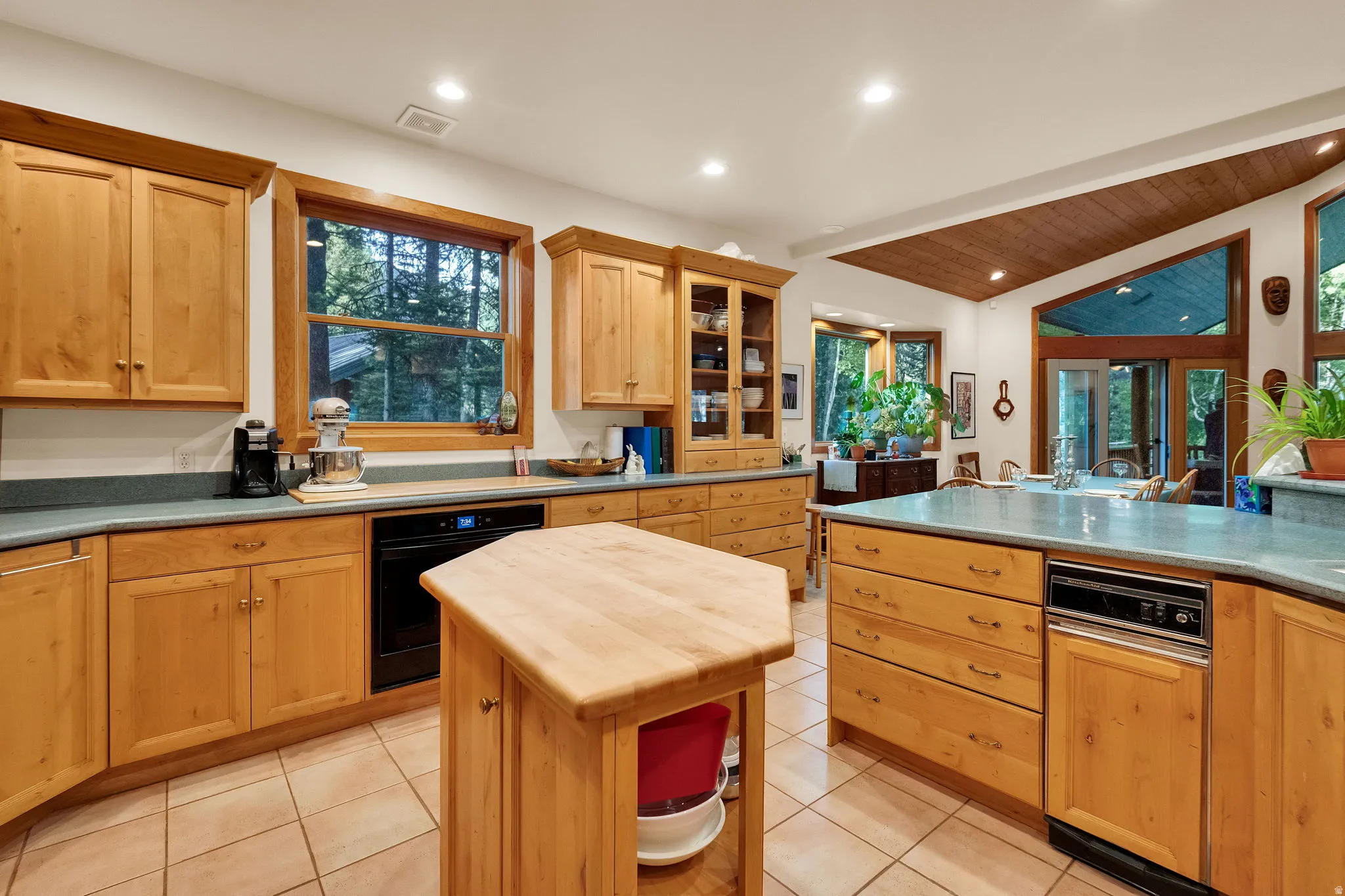 Kitchen featuring light wood cabinetry, light blue countertops, a central island with a wood countertop, integrated dishwasher, and tiled flooring