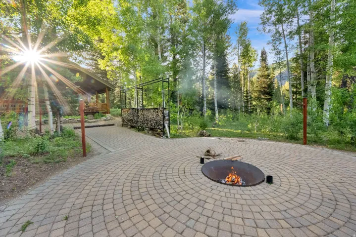 Circular paver patio with a built-in fire pit, surrounded by mature trees
