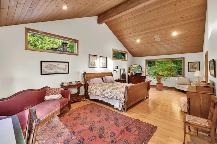 Spacious room featuring vaulted wood-paneled ceilings, warm wood-finish flooring, and white walls