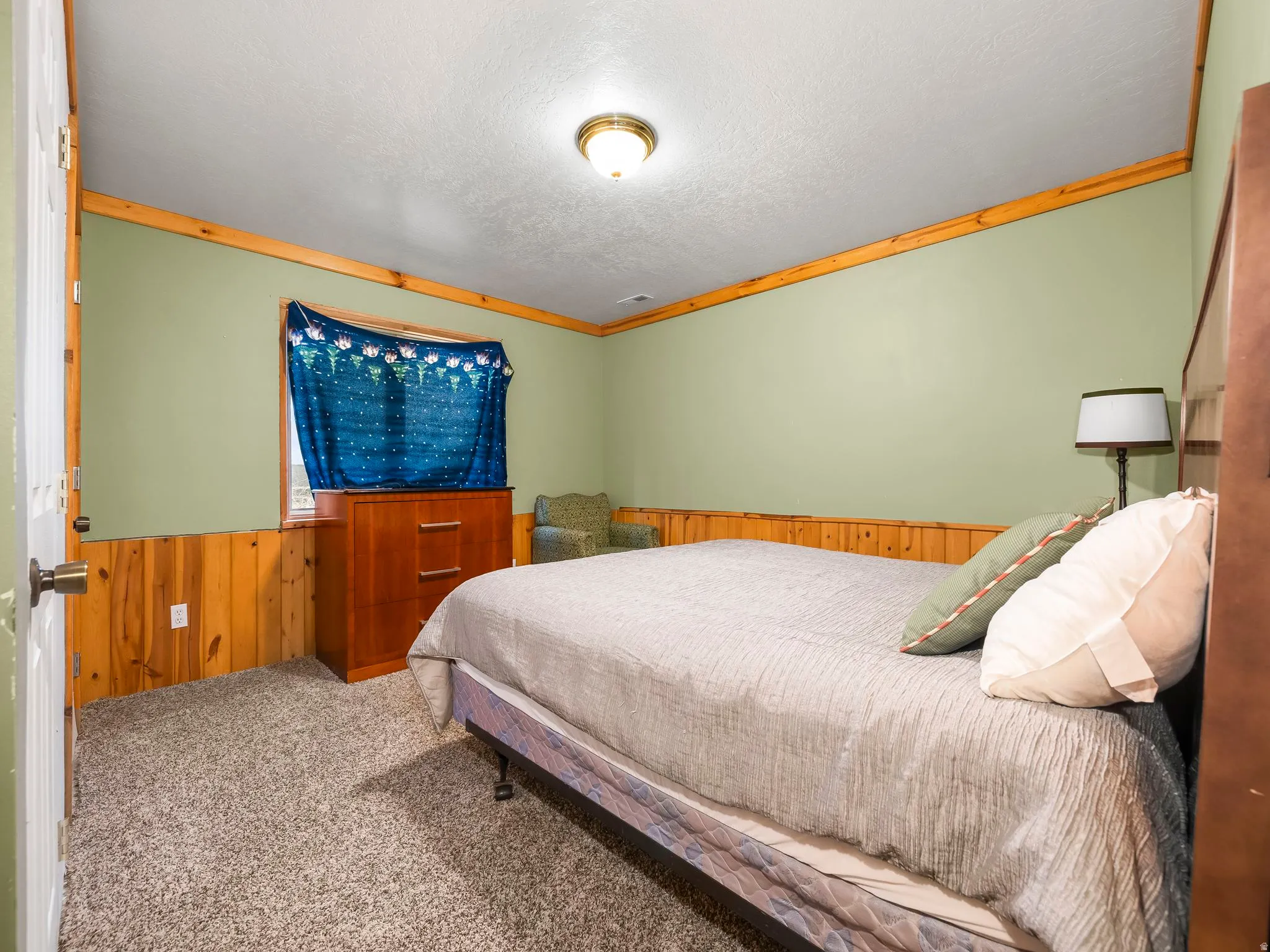 Bedroom featuring wooden walls, wainscoting, crown molding, carpet flooring, and a textured ceiling