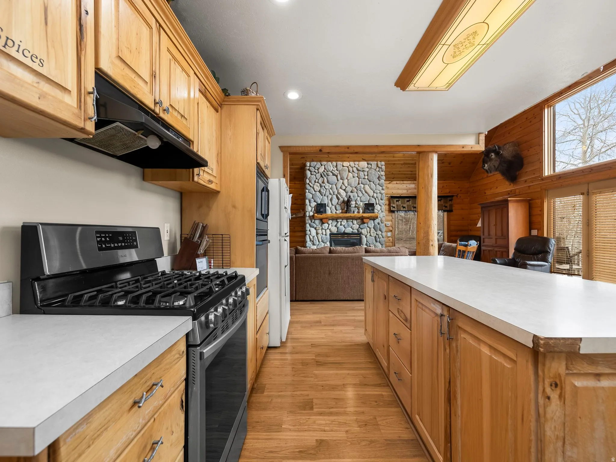 Kitchen featuring black appliances, open floor plan, a stone fireplace, light countertops, and light wood-style floors