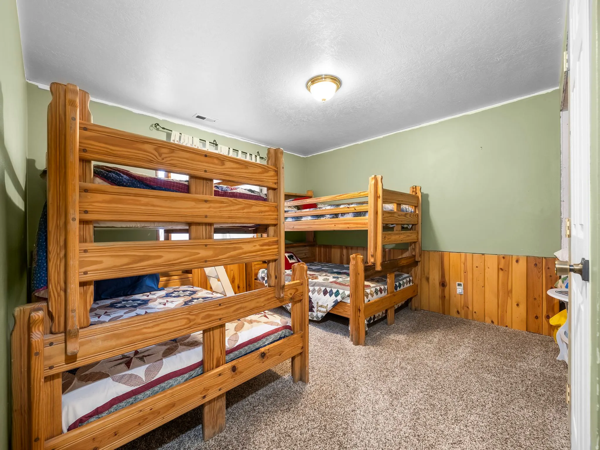 Bedroom with wooden walls, a wainscoted wall, light colored carpet, and a textured ceiling