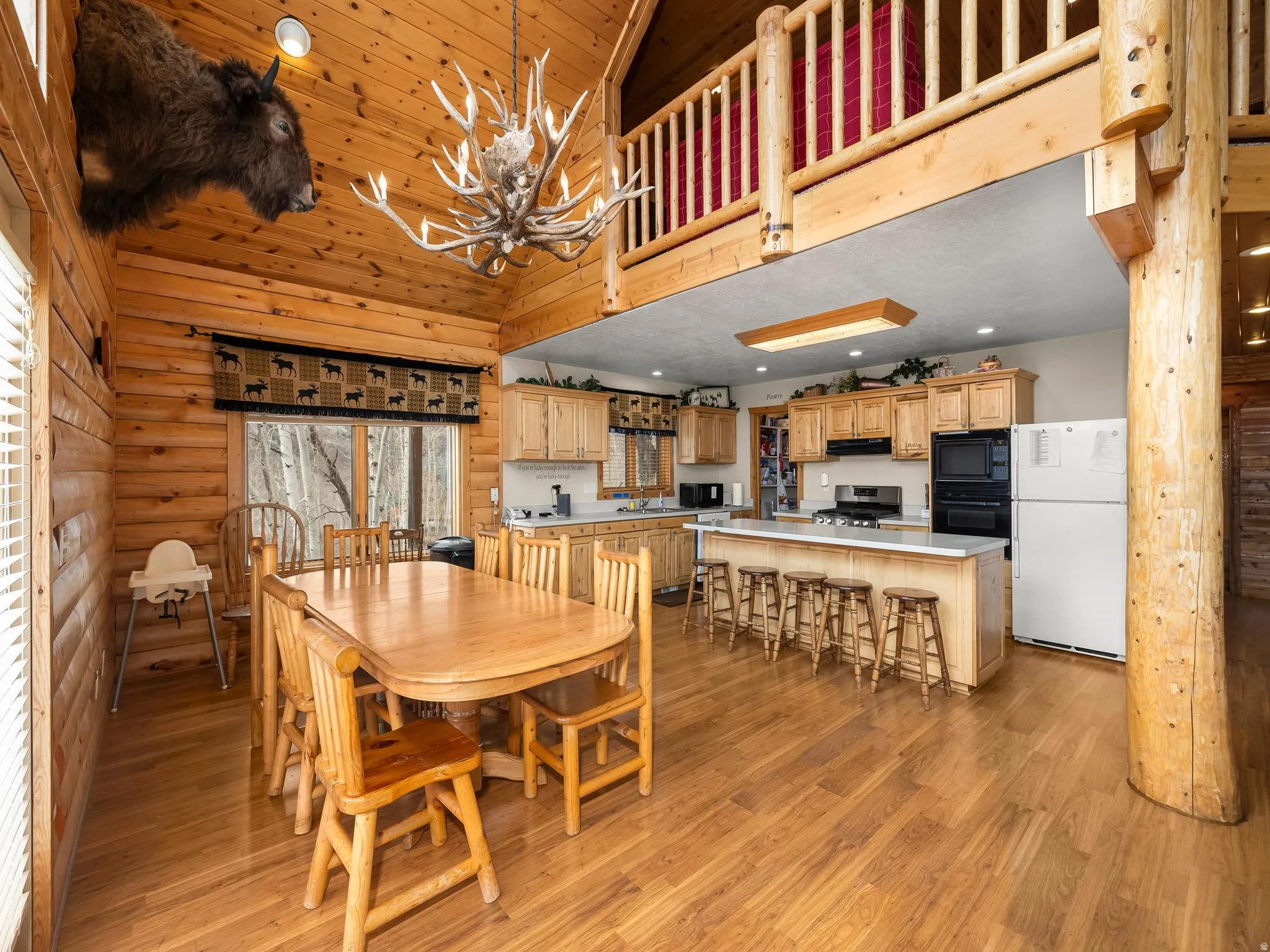 Dining room with rustic walls, hanging lights, light wood-type flooring, and vaulted ceiling