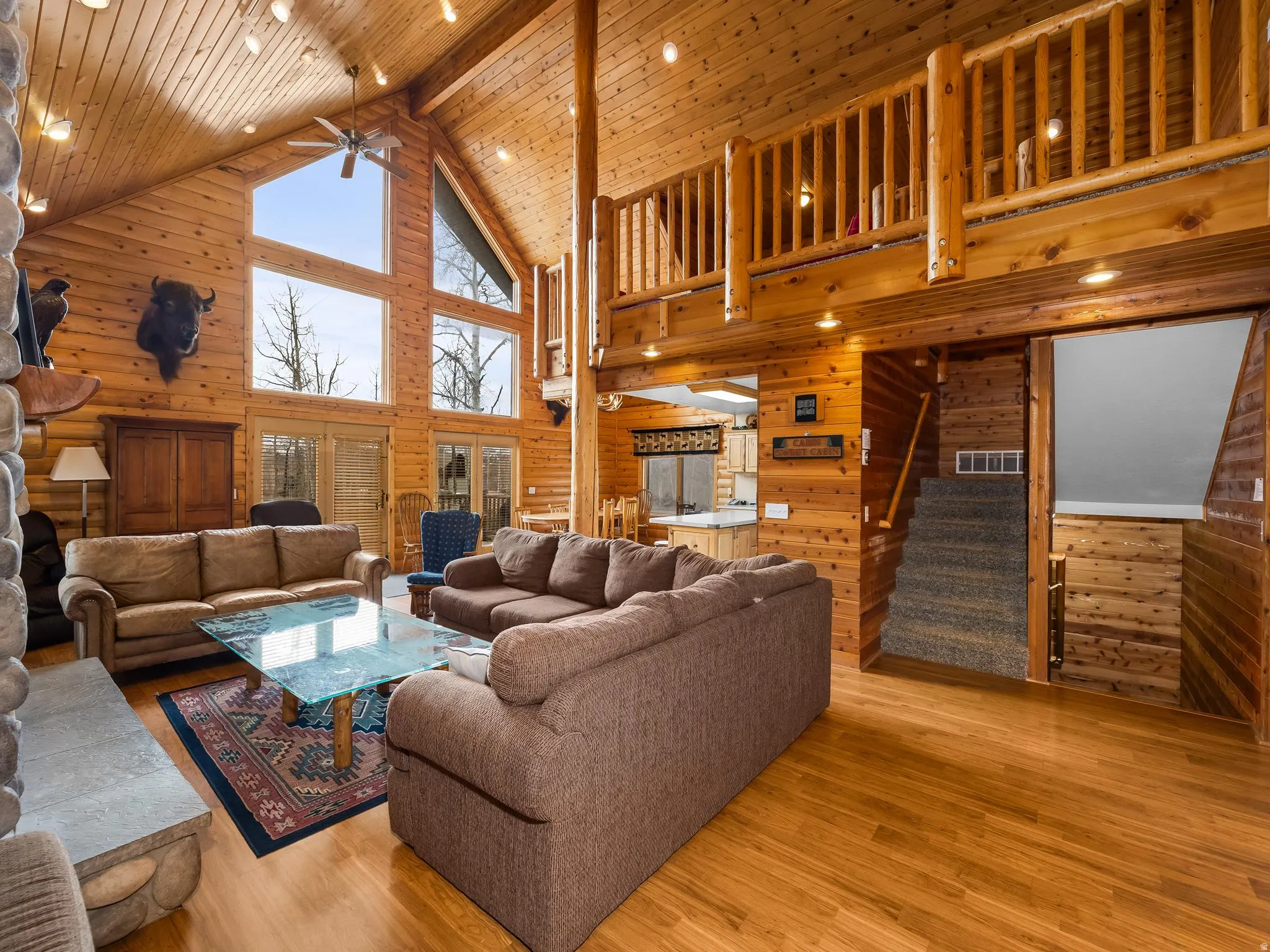 Living room featuring wooden walls, wood finished floors, a ceiling fan, and a high wooden beamed ceiling