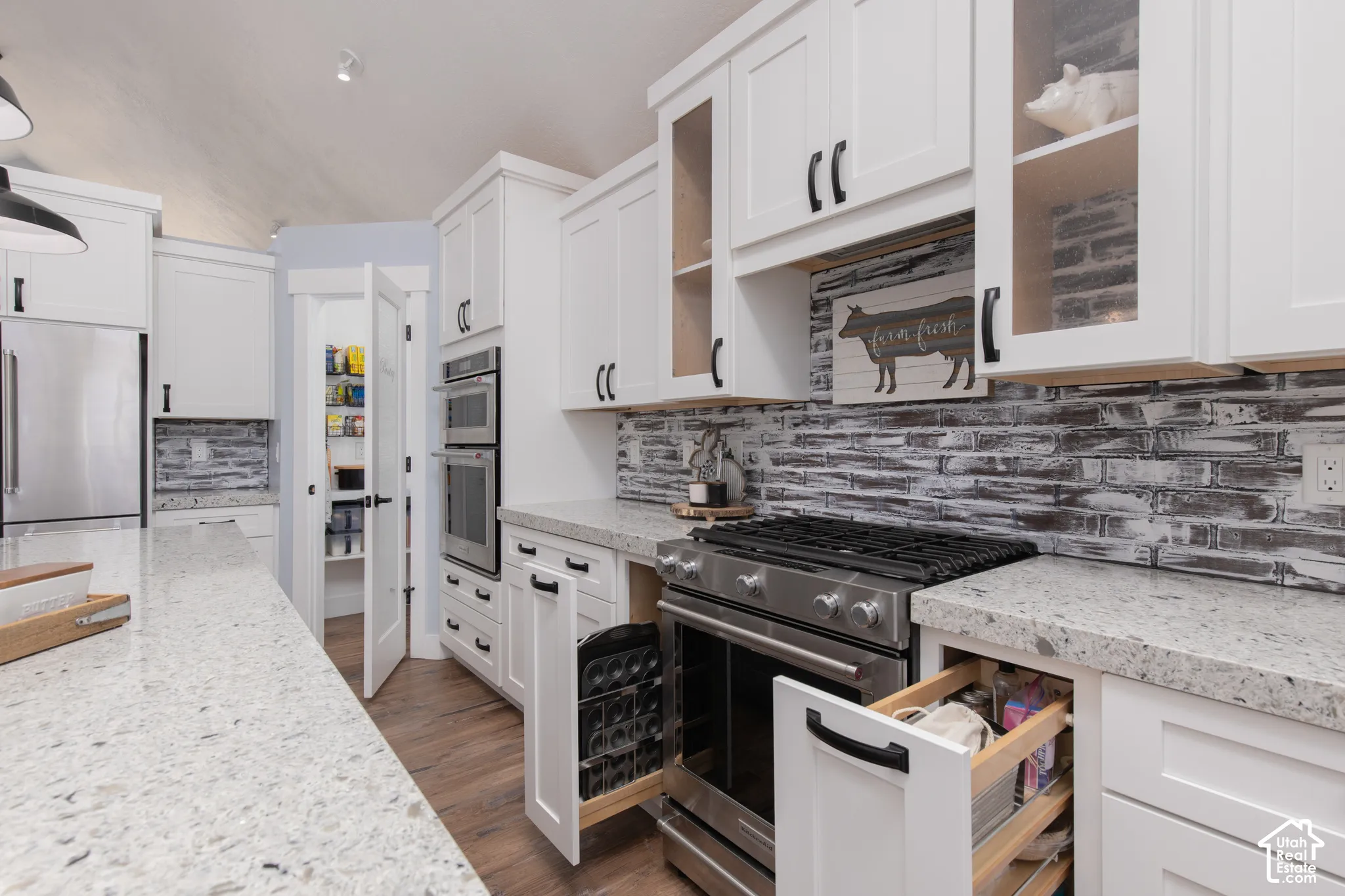White shaker cabinetry, stainless steel appliances, stone countertops, wood-finish flooring, and a brick-style backsplash