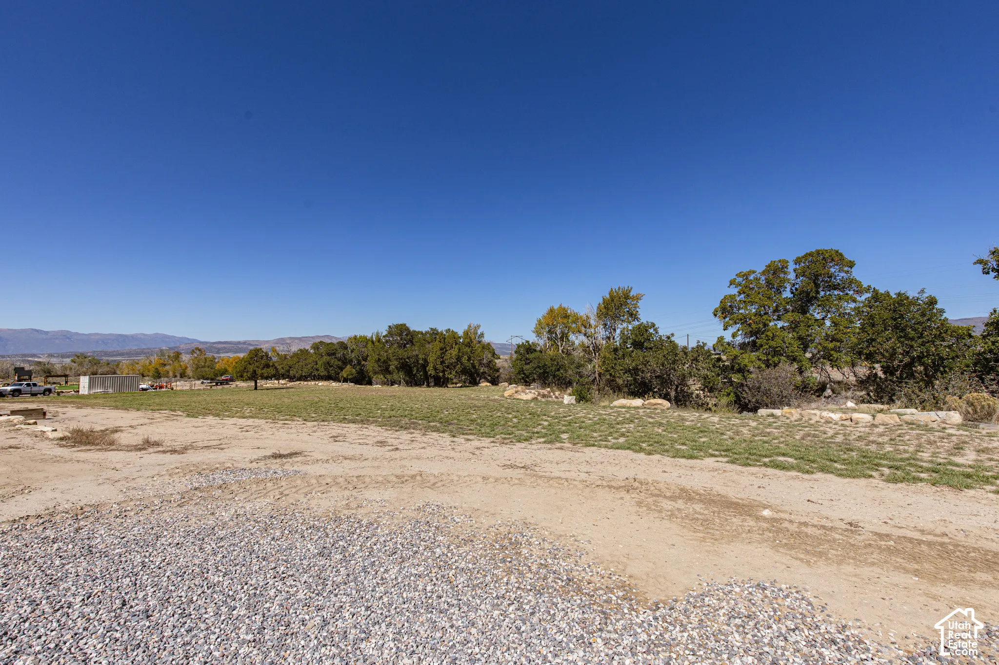 Expansive land parcel featuring partial gravel coverage and established trees