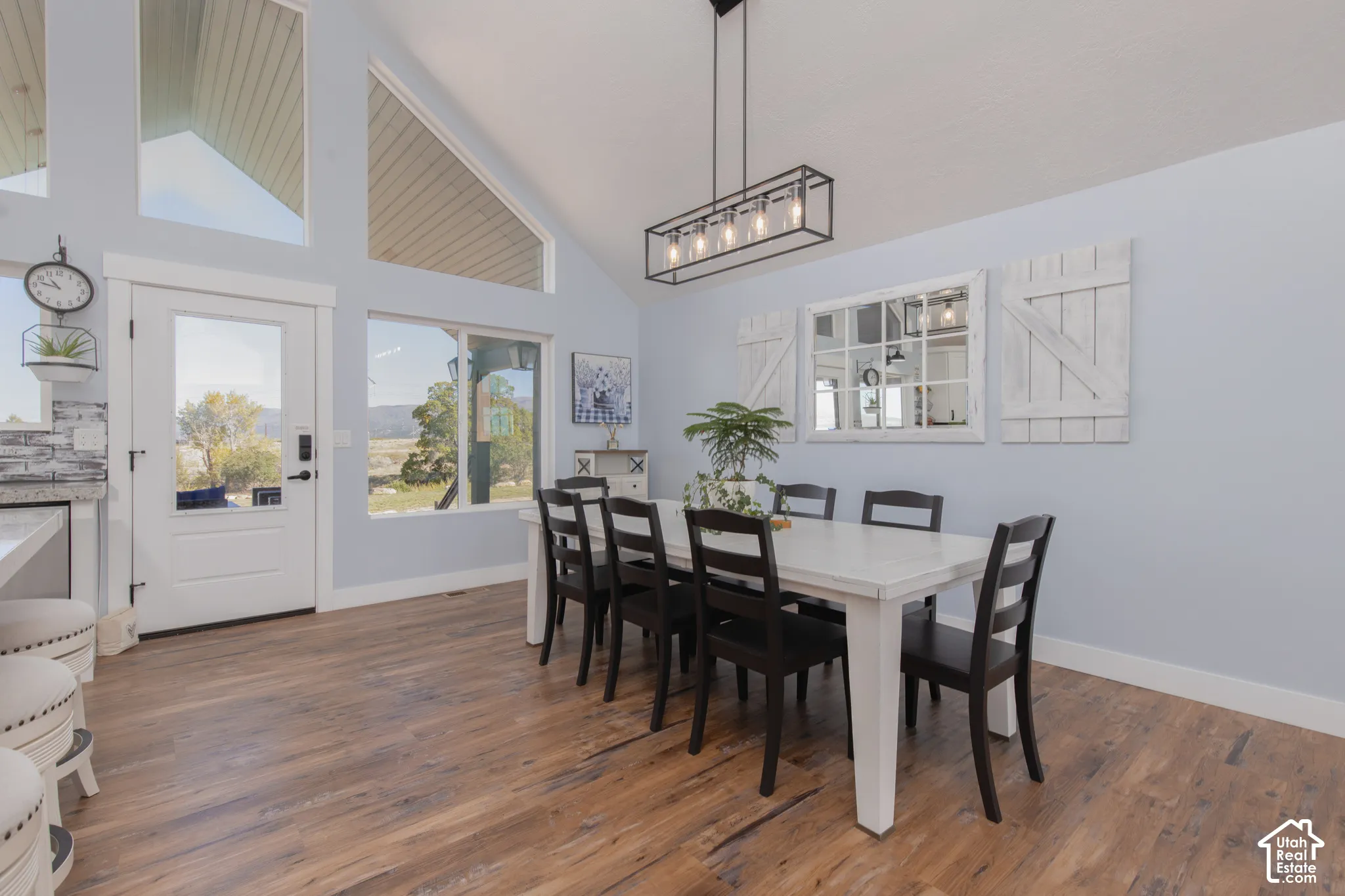 Vaulted ceiling with high windows, wood-finish flooring, glass-paneled exterior door, linear chandelier, and light blue wall finish