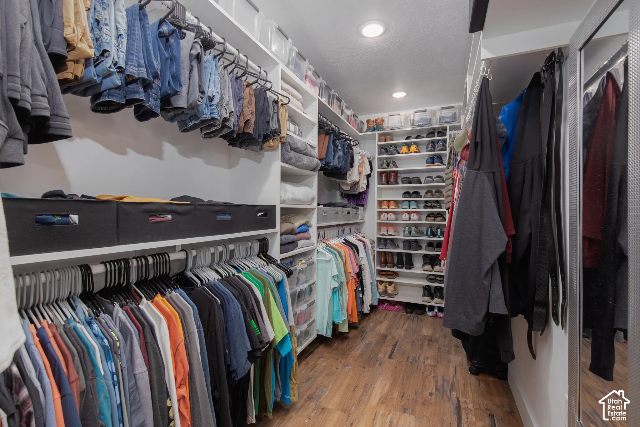 Custom closet organization system with wood-finish flooring, recessed lighting, and mirrored closet doors