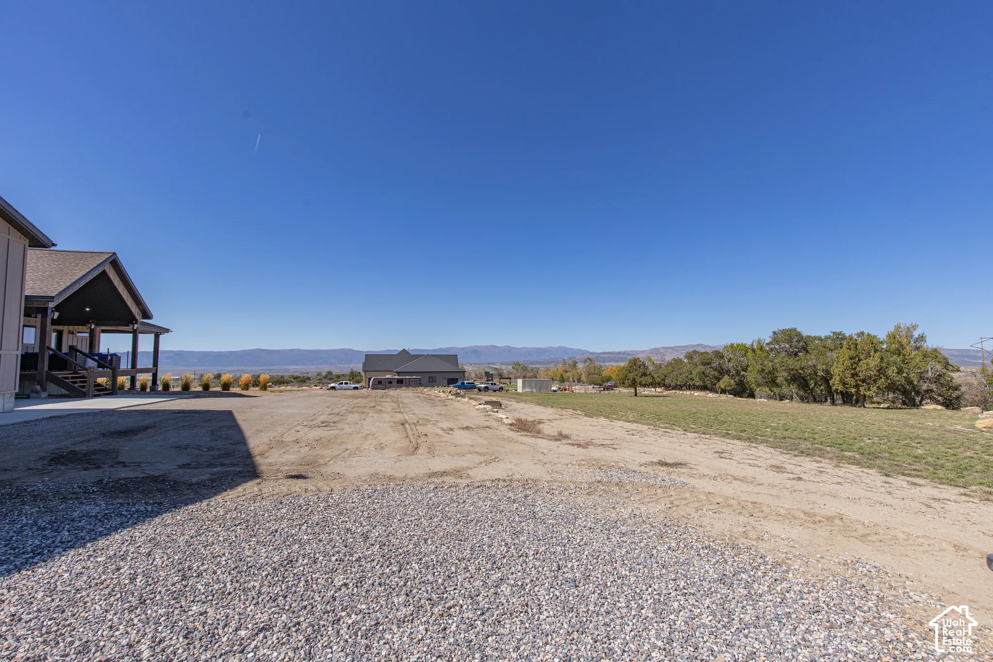 Expansive gravel and dirt lot featuring a partial house exterior with covered porch