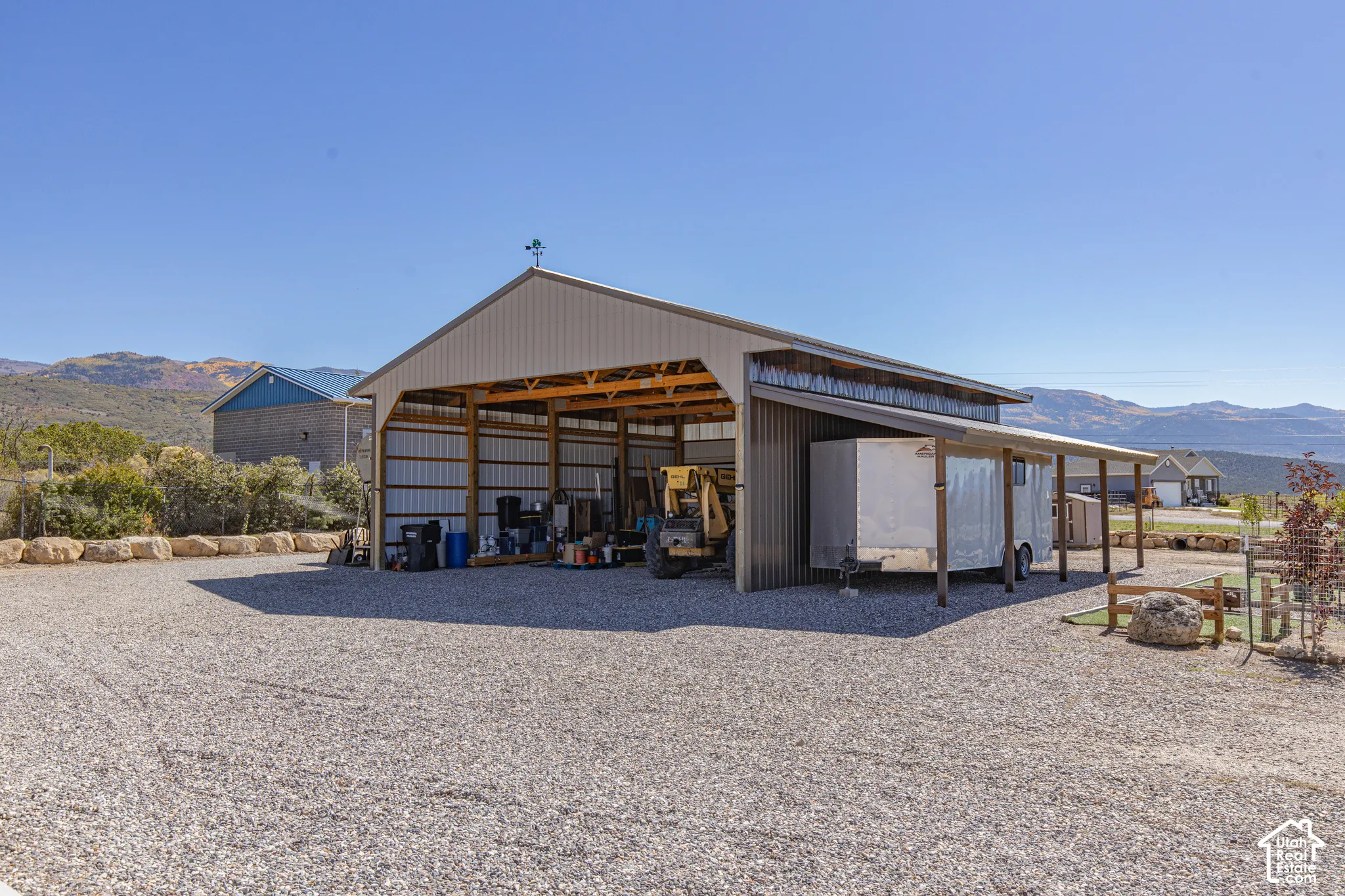 Expansive gravel lot with a large metal-sided outbuilding featuring an open-sided storage bay and an attached covered lean-to