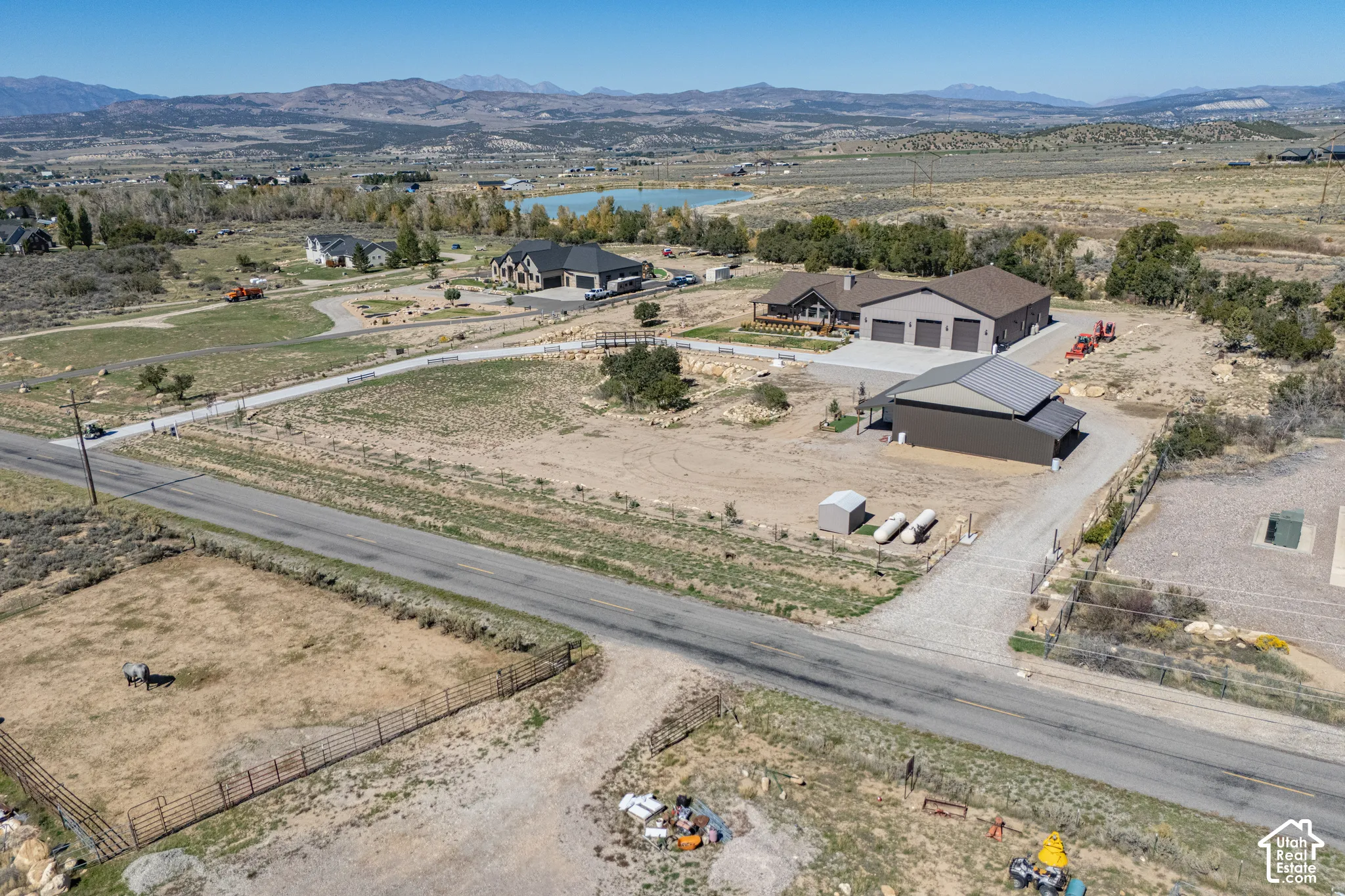 Main residence featuring a multi-car garage, separate outbuilding with solar panels, gravel driveways, and an adjacent fenced pasture