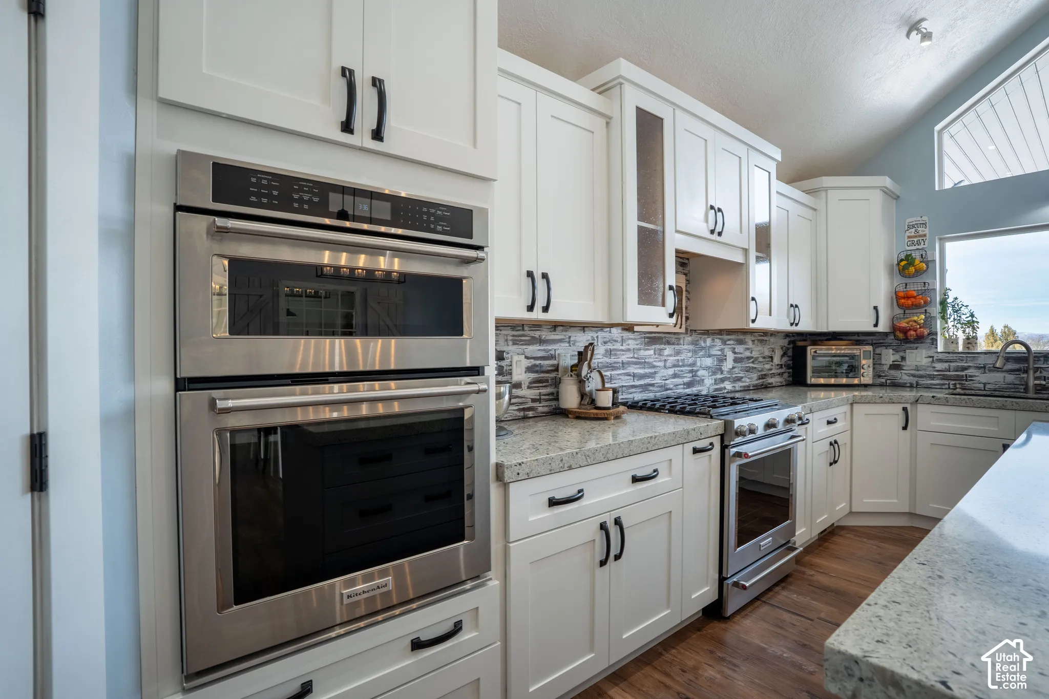 Kitchen with stainless steel appliances, white cabinetry, decorative backsplash, light stone countertops