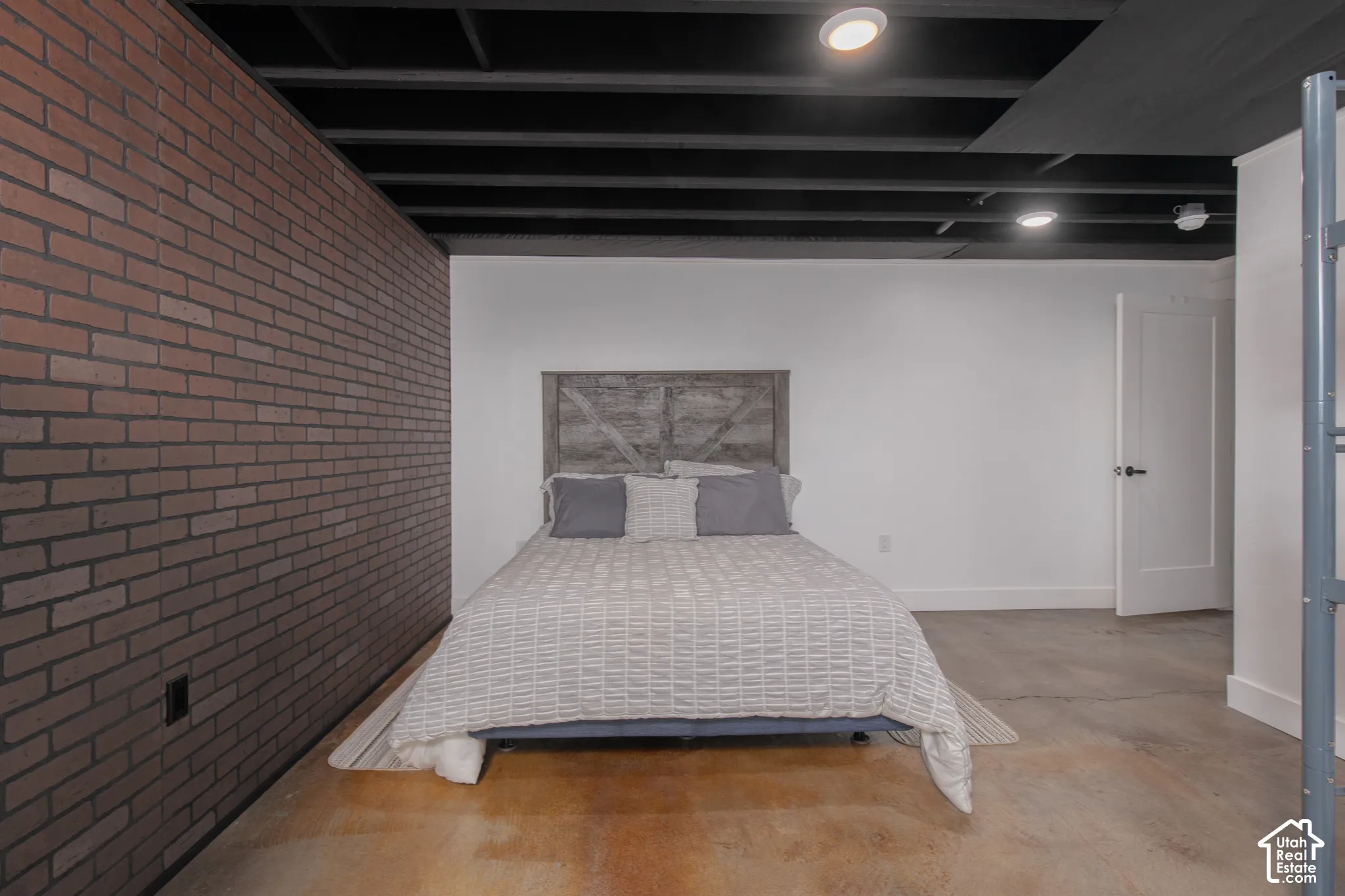 Exposed brick wall, concrete flooring, recessed lighting, white panel door, and dark exposed ceiling beams