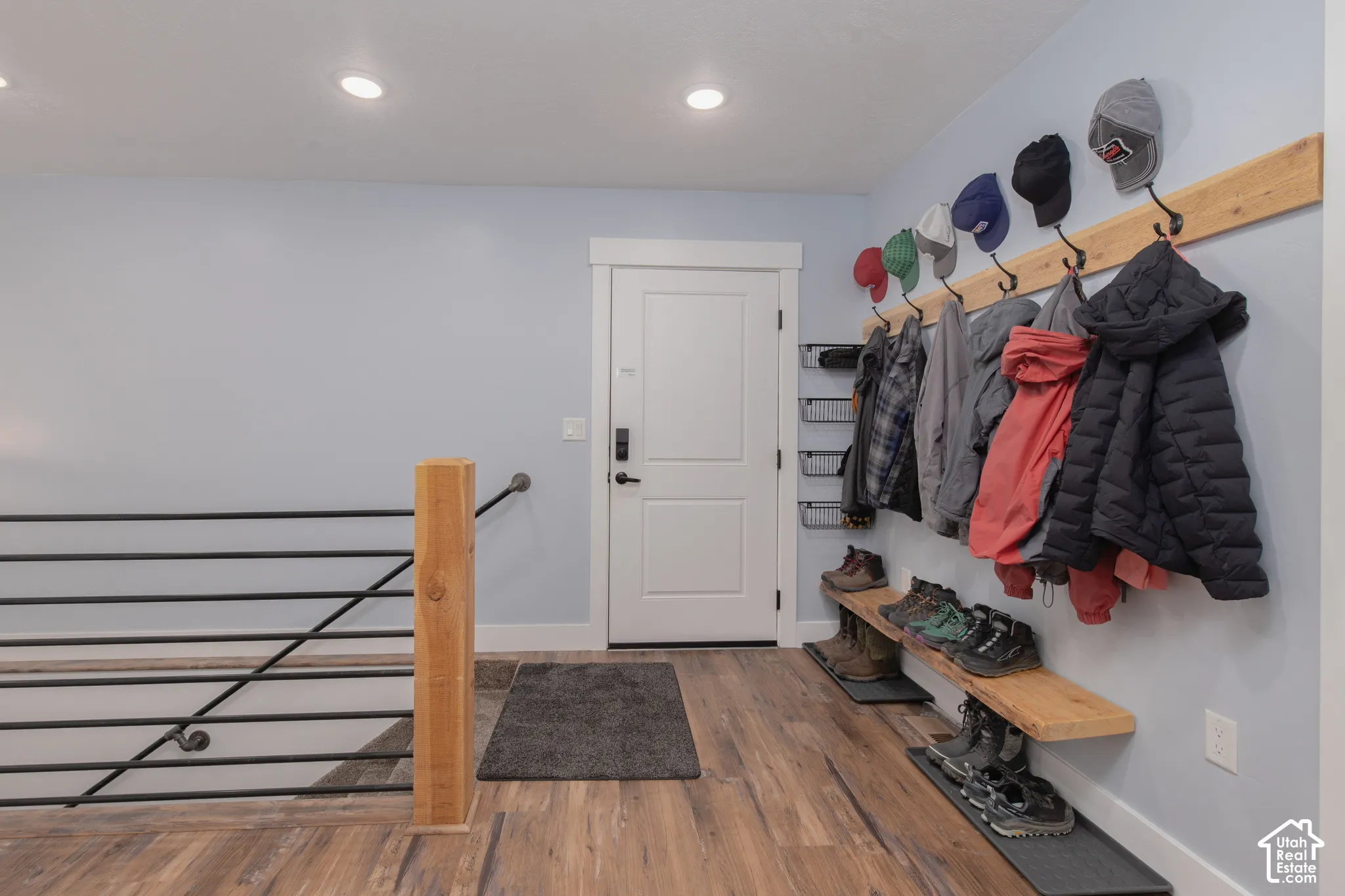 Recessed ceiling lighting, wood-finish flooring, white door, light blue wall paint, and a wood and black metal railing