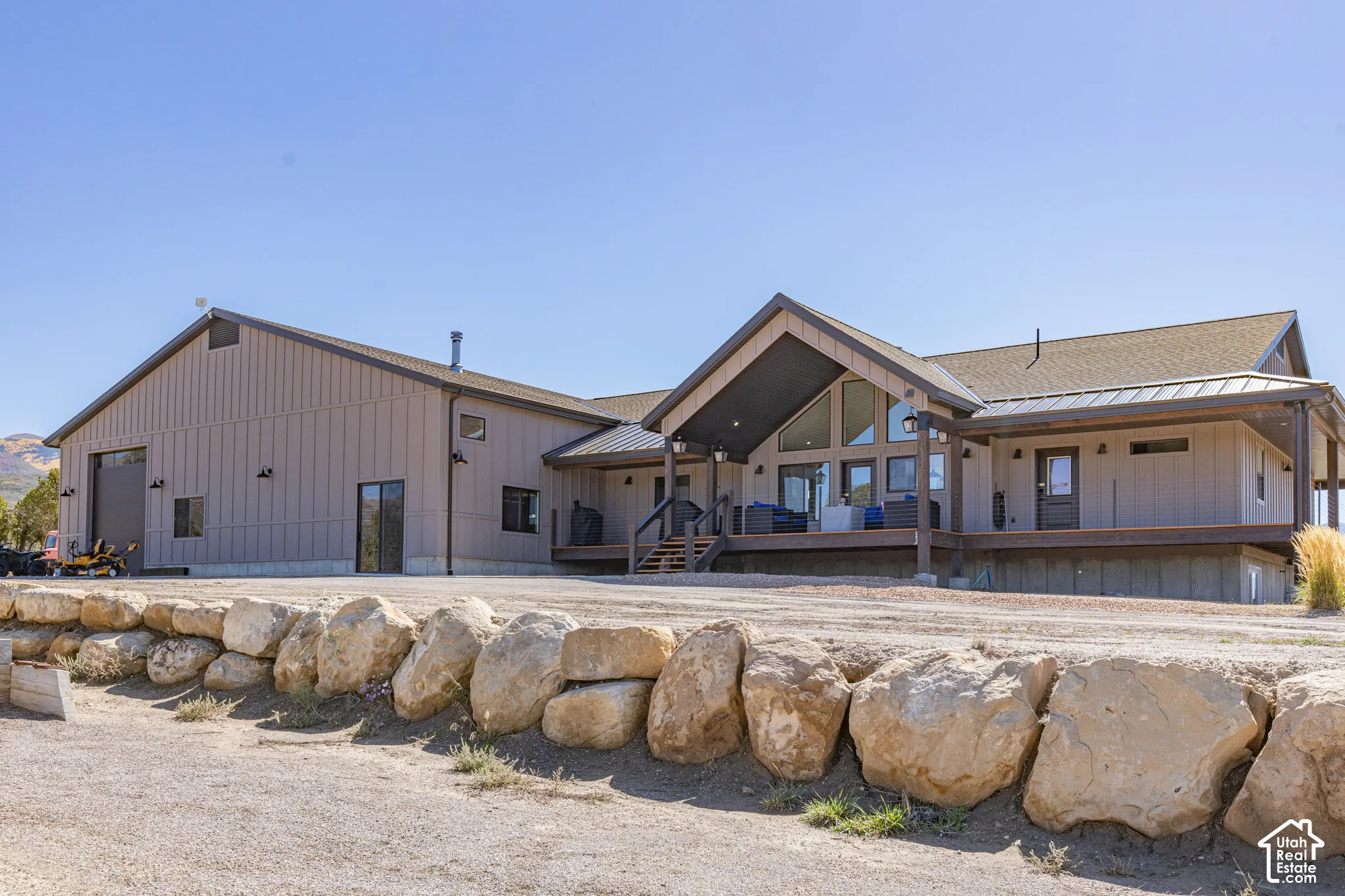 Expansive exterior featuring a natural stone retaining wall, multi-level decking, large window banks, and a dedicated garage with a roll-up door